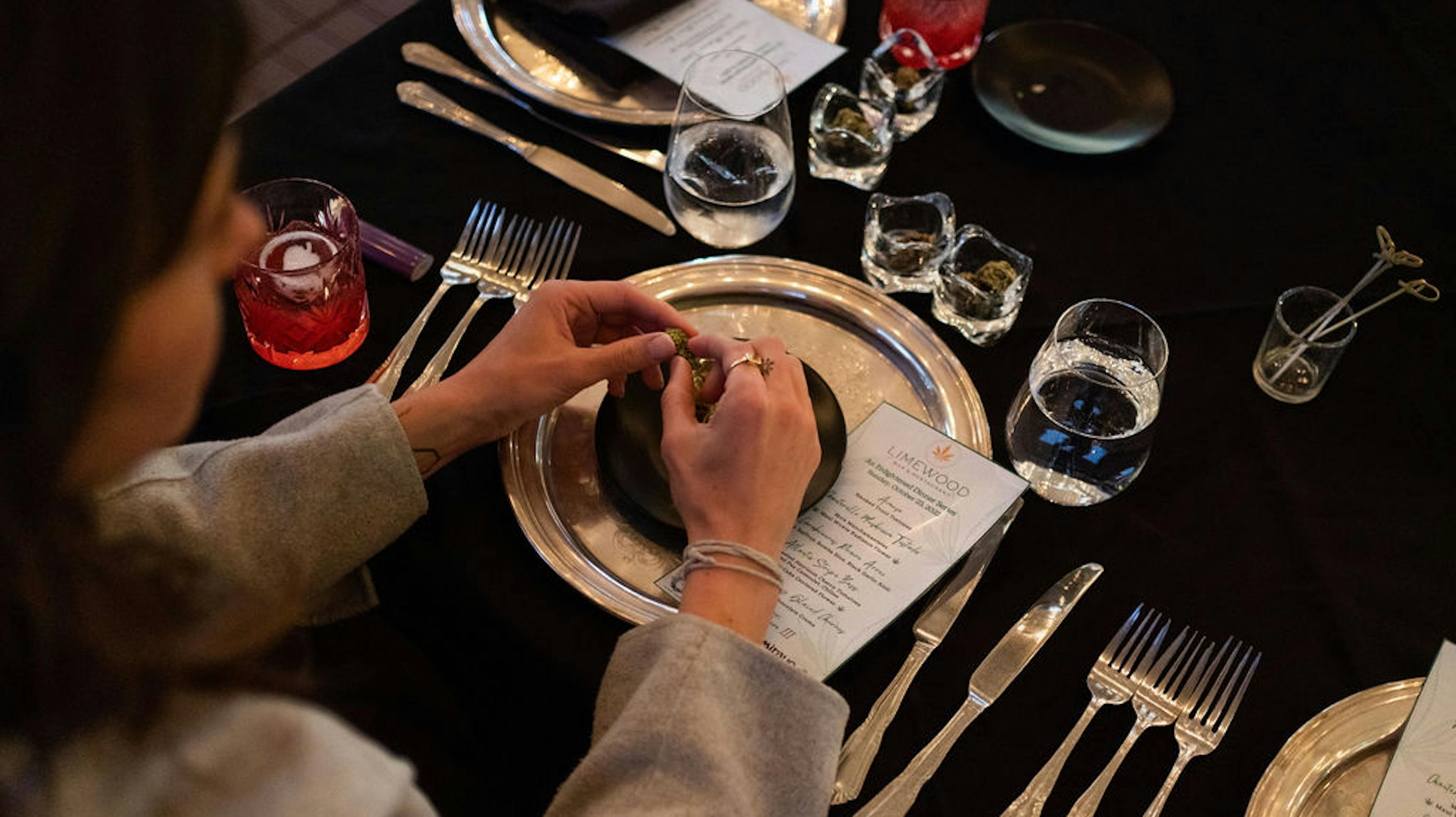 A guest breaking up a nugget of Mirayo flower at her seat, with a full set of silverware and glassware. 