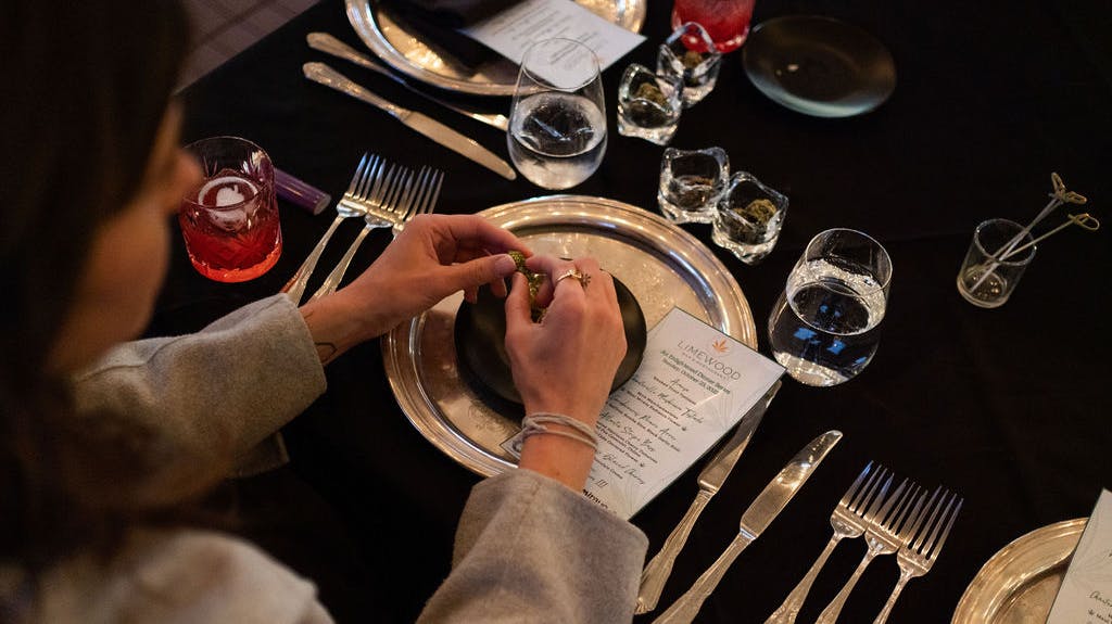 A guest breaking up a nugget of Mirayo flower at her seat, with a full set of silverware and glassware. 