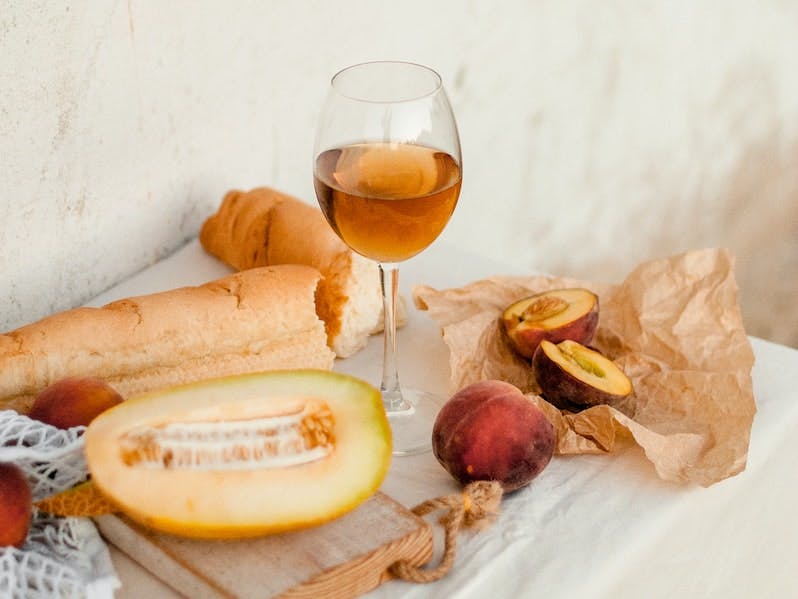 A lovely spread of orange wine, baguette, cantaloupe, and peaches. 