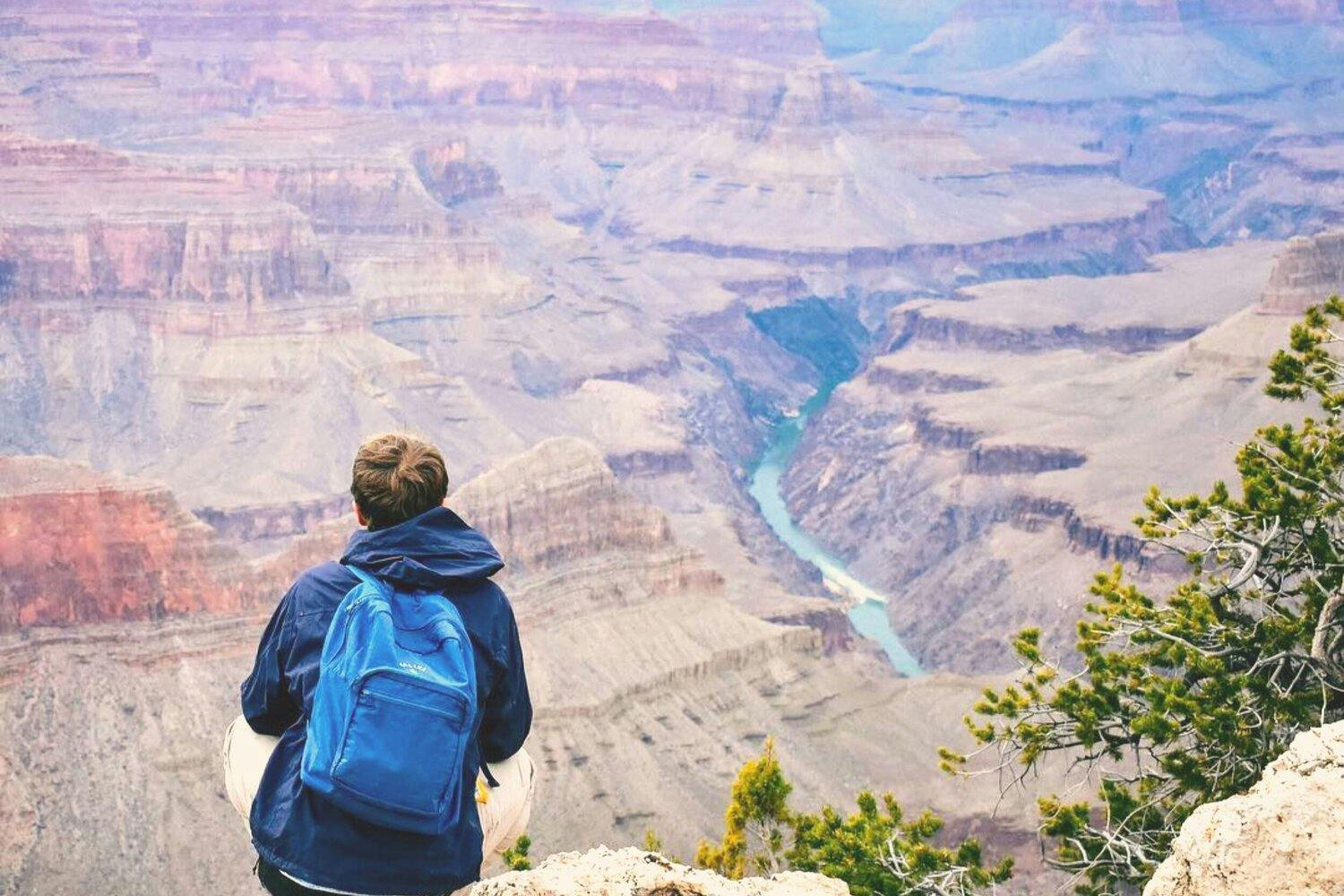 Man in blue Caliva backpack kneeling on the edge of the Grand Canyon.