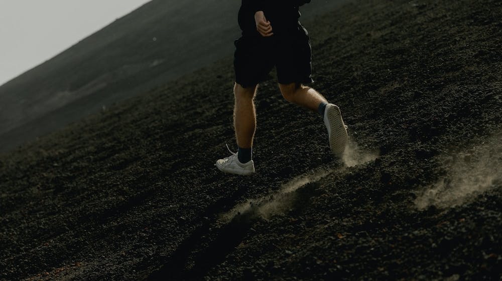 A man is running in sneakers on top of what appears to be volcanic rock.