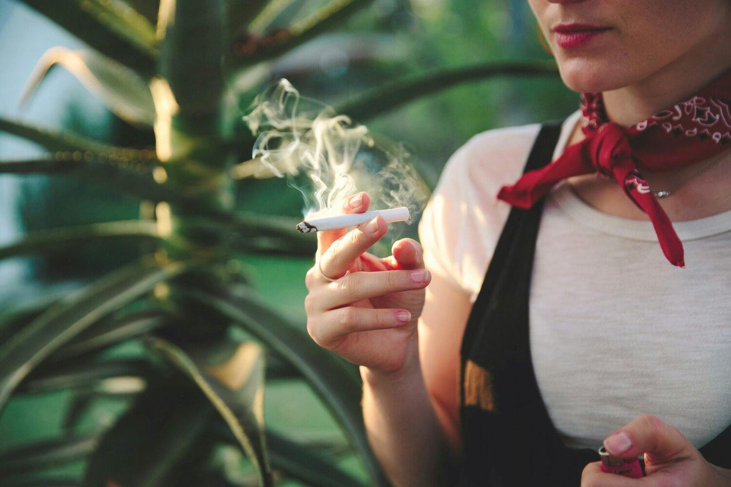 A woman in a red scarf holding a lit marijuana cigarette.