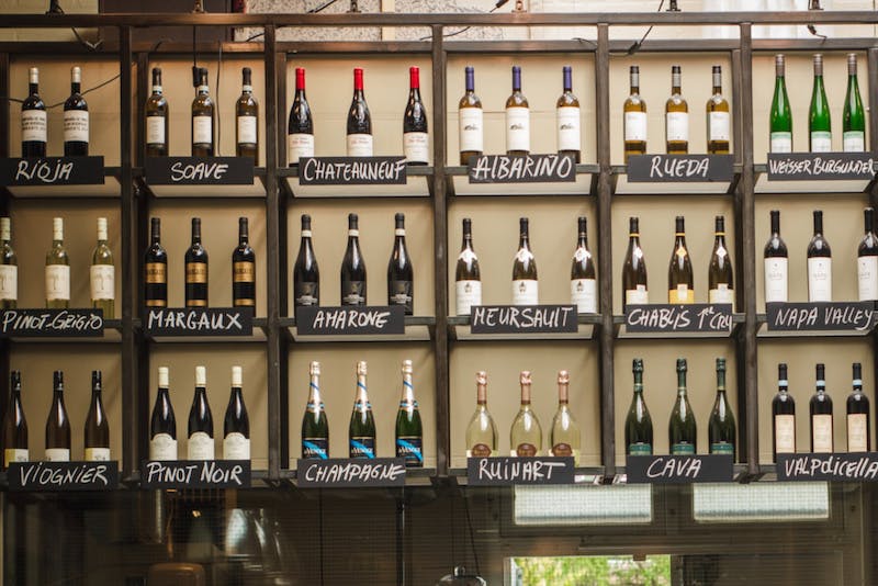 An assortment of wine bottles displayed with names on an overhead shelf. 