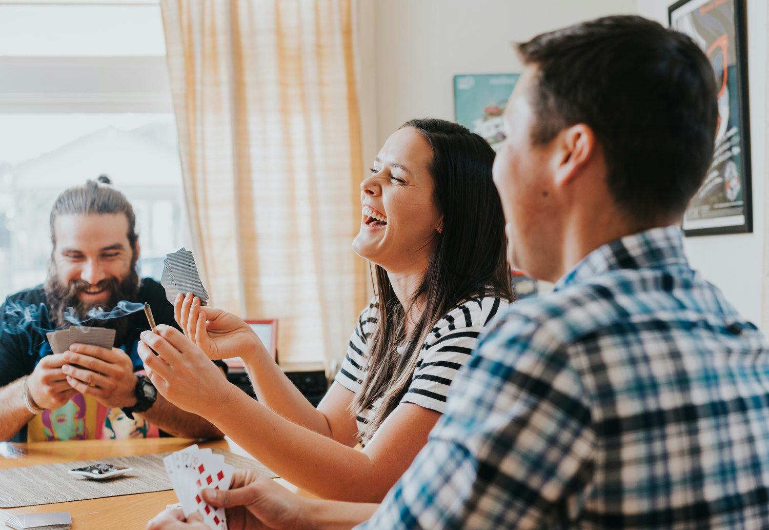 A woman and two men sitting around a table laughing while playing a card game.