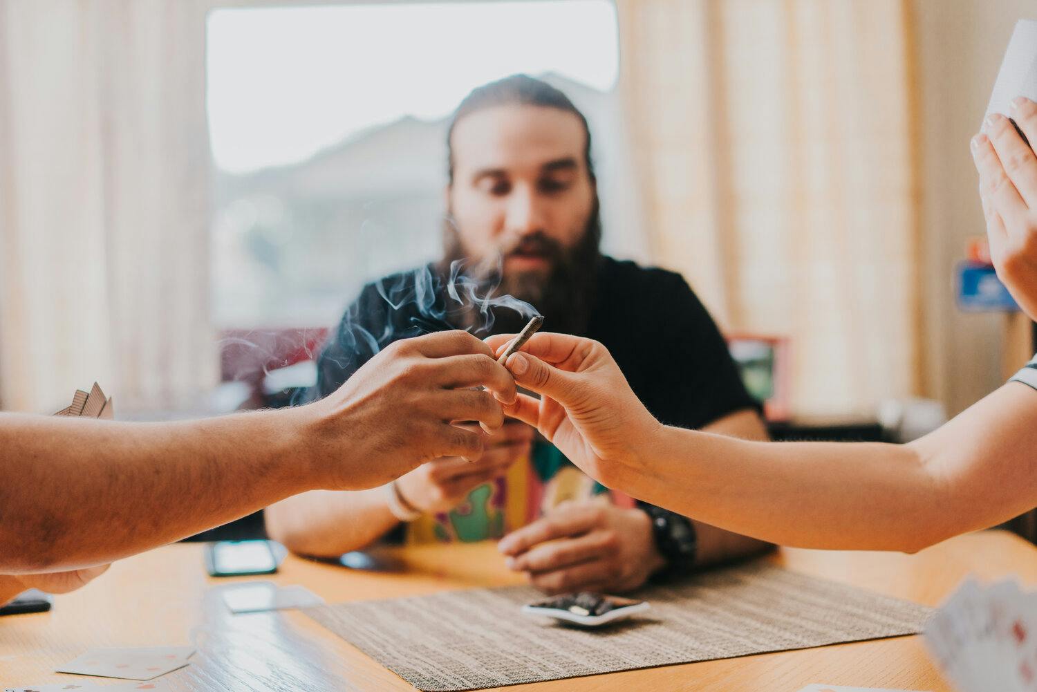 3 people passing a joint around at a card game.