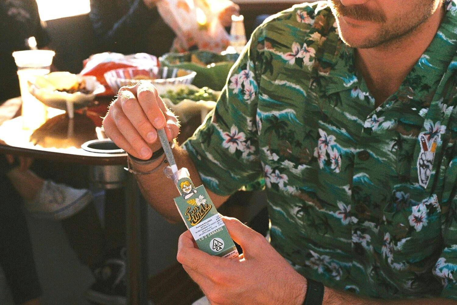 Man in a green Aloha shirt pulling out a Fun Uncle cannabis pre-roll.