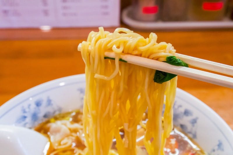 Chopsticks pick up a glorious chunk of thick ramen noodles from a bowl. 