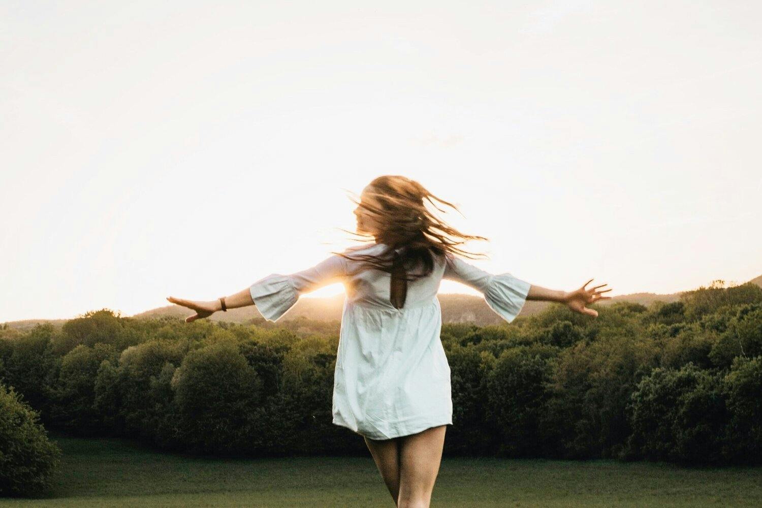 Woman in white dress standing in a field with arms out wide.