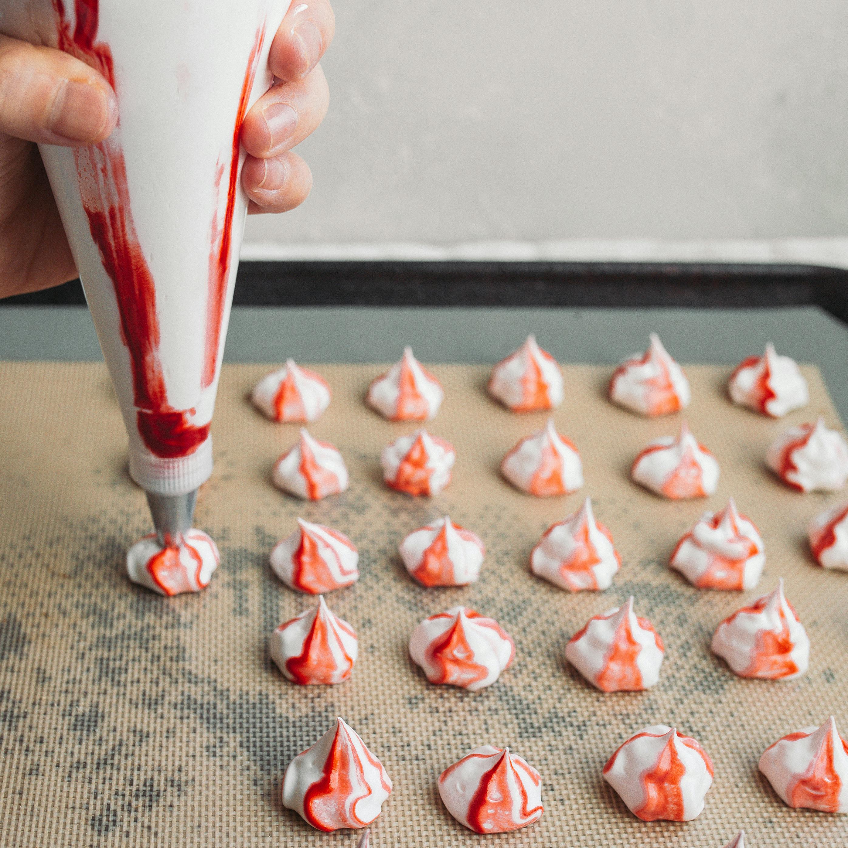 Woman holding piping bag making red and white weed-infused meringues.