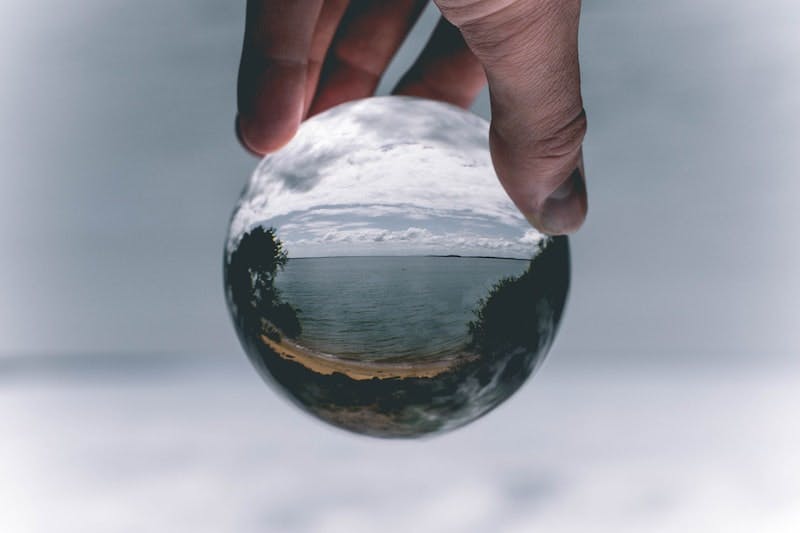 A hand holds a glass globe reflecting a beautiful lake scene.