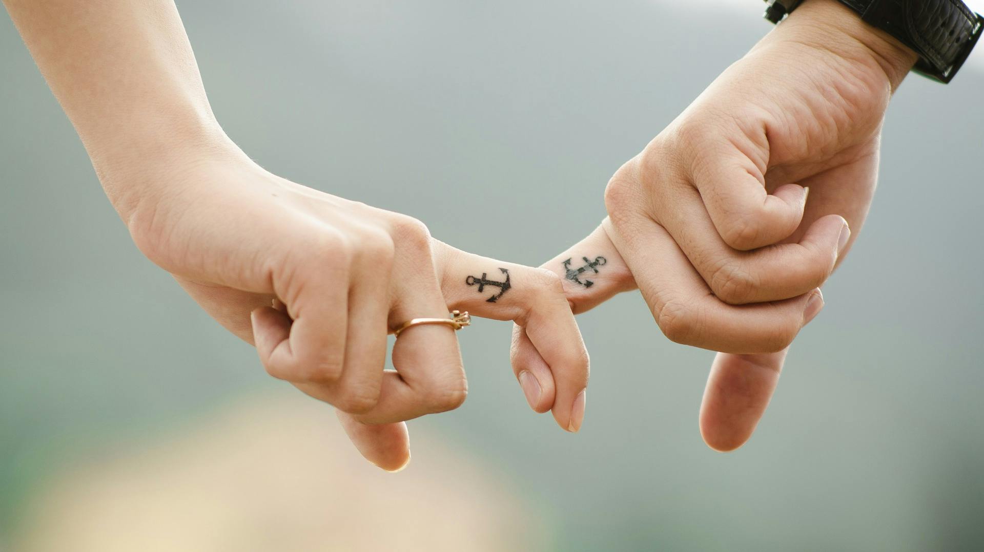 Couple with anchor finger tattoos holding hands