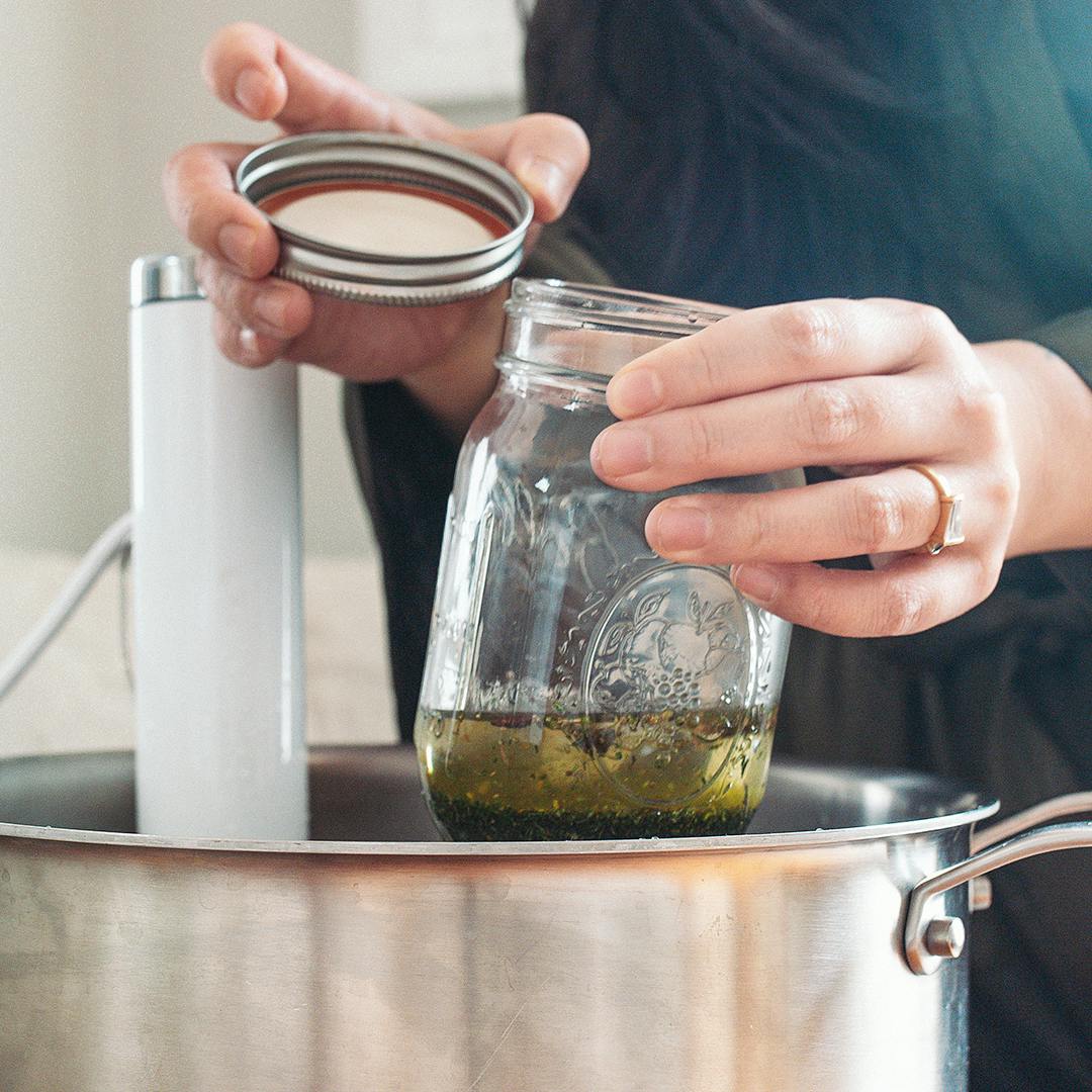 Woman putting mason jar of cannabis oil in sous vide pot.