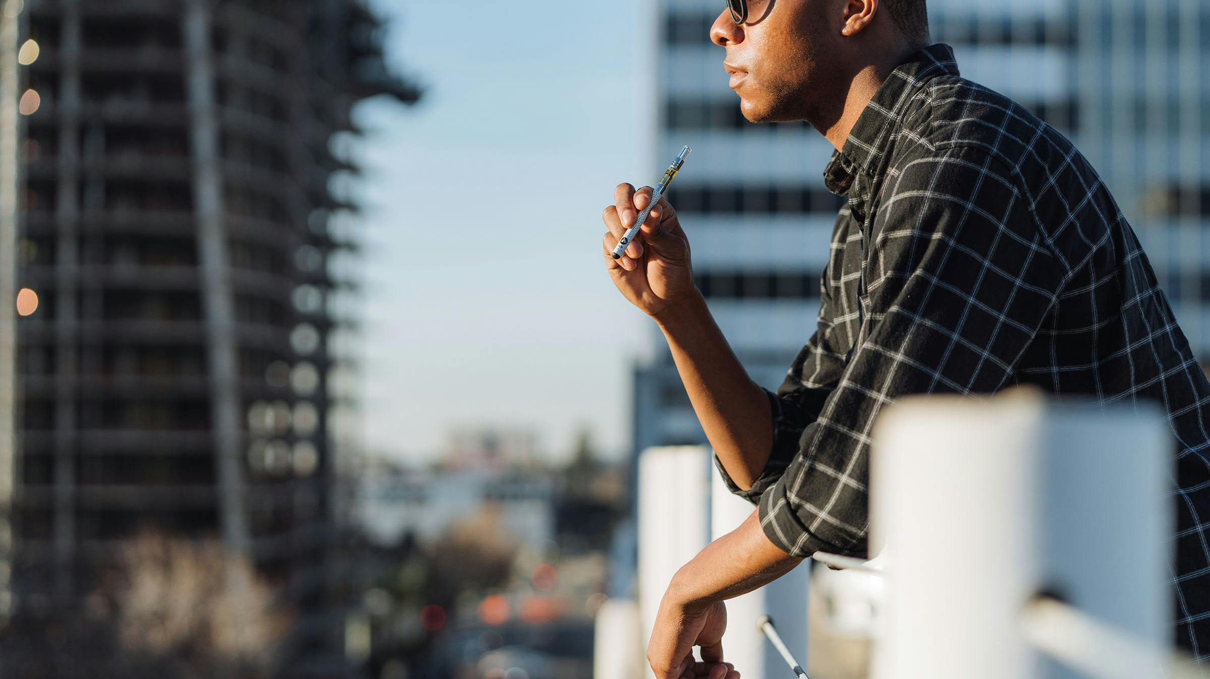 Man standing on balcony holding a Caliva cannabis vape pen.