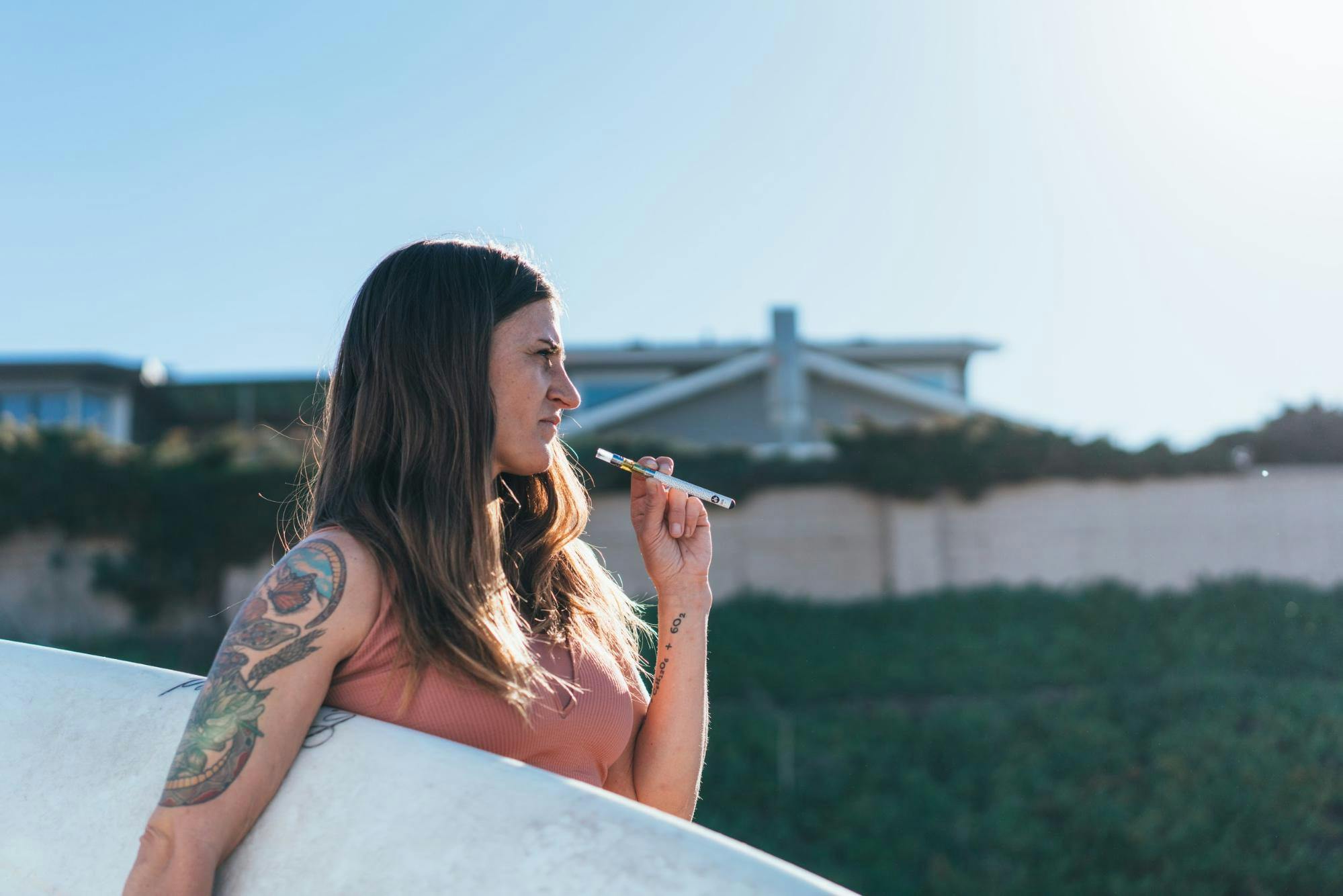 woman holding a surfboard under her arm and a vape in the other arm 