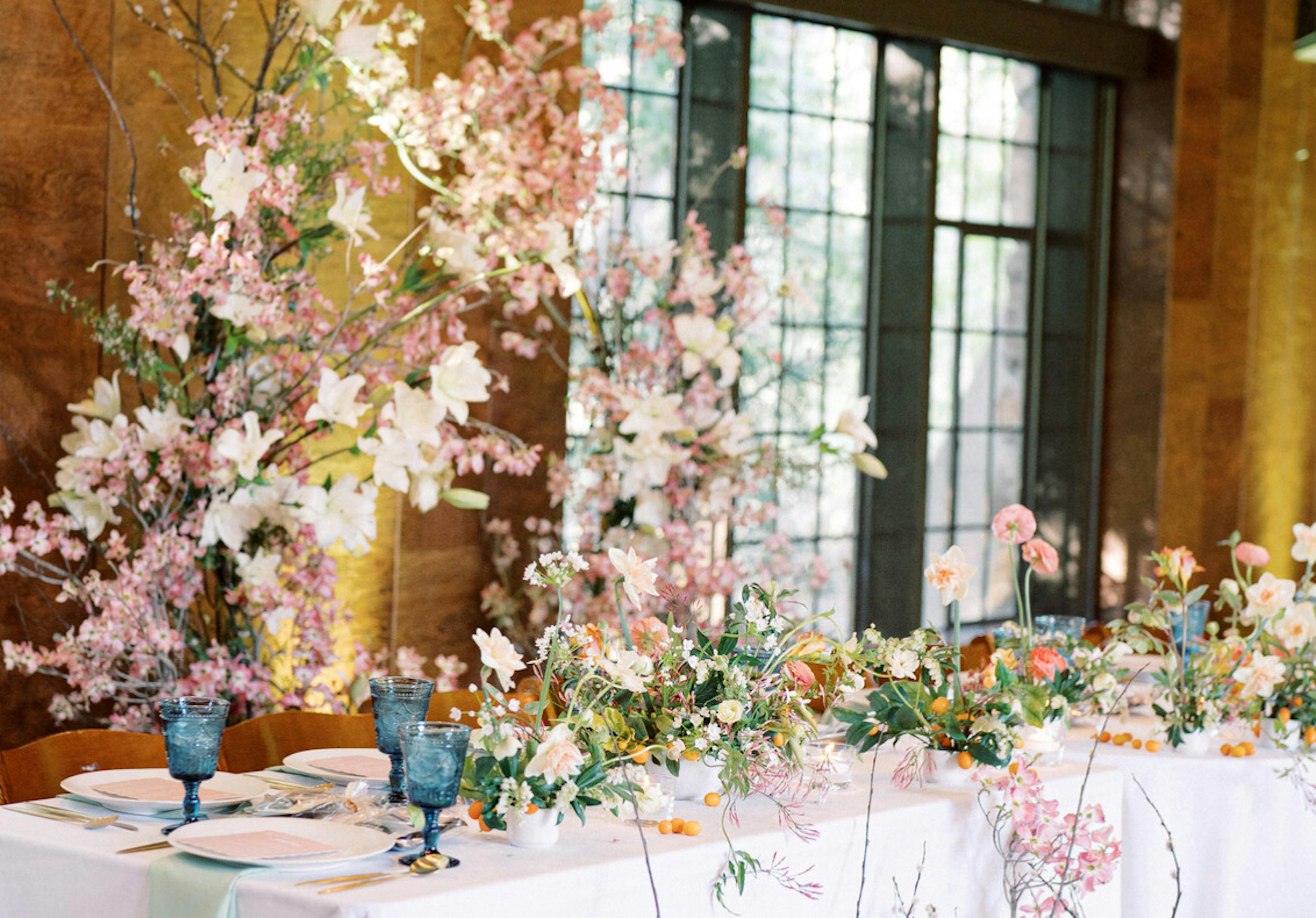 A reception sweetheart table adorned with flowers and table settings with a floral arch in background.