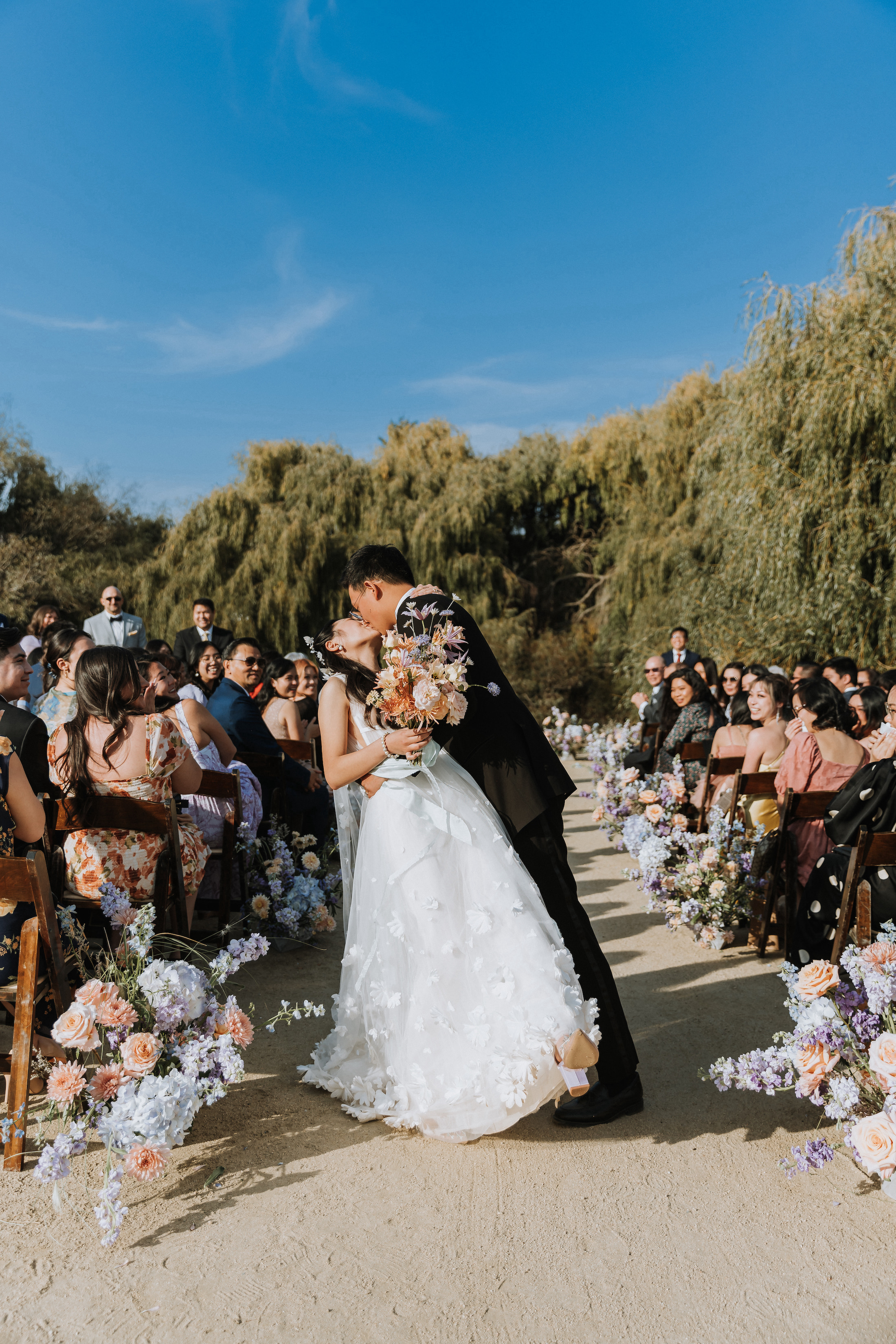 Bride and groom share a kiss in the middle of the aisle lined with florals to conclude their wedding ceremony.