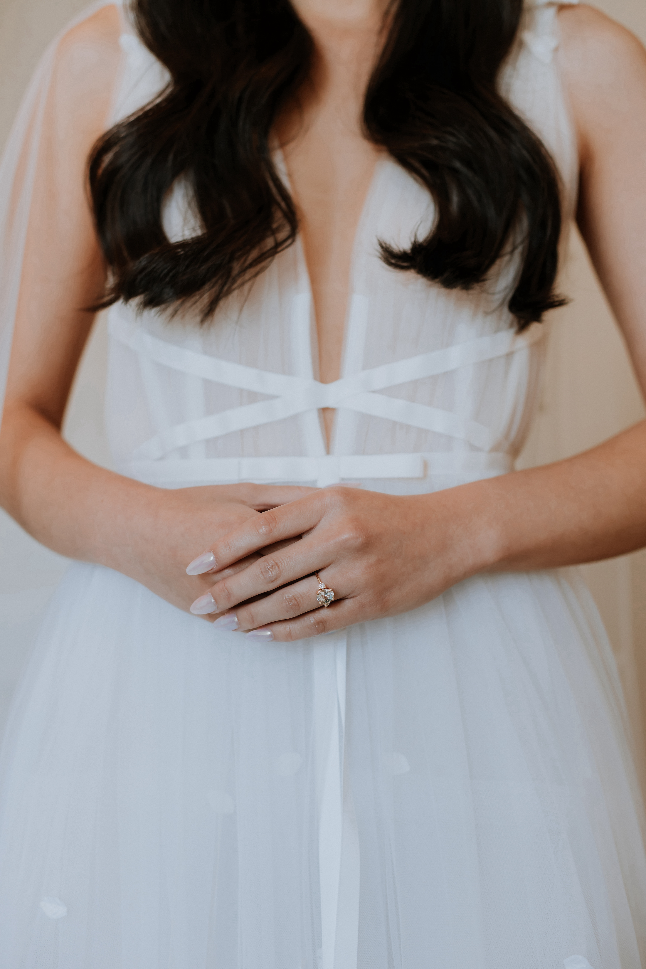 Close up of a bride in a white wedding gown standing with her hands clasped together.