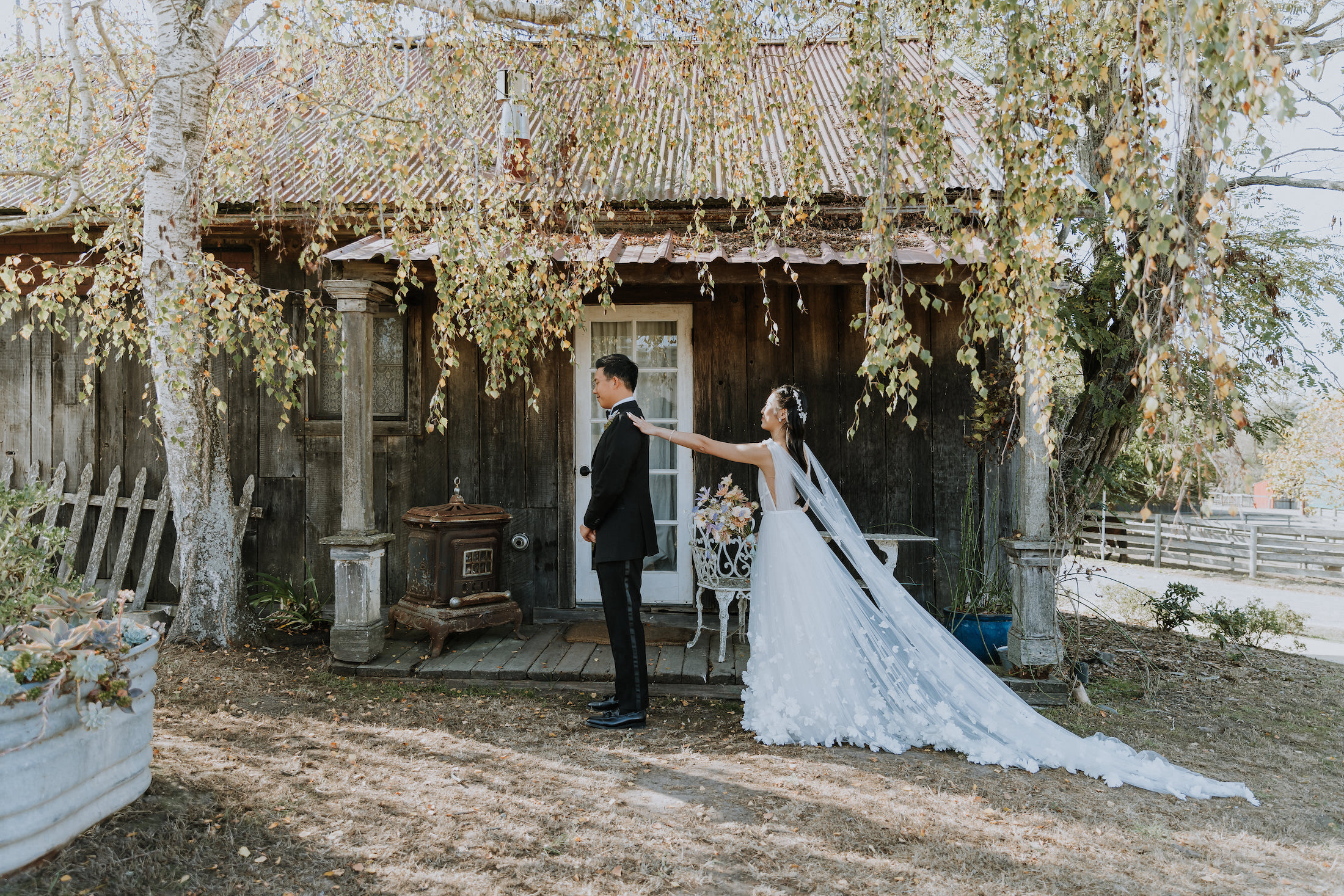 A bride tapping on the groom's shoulder about to share their first look in front of a rustic barn.