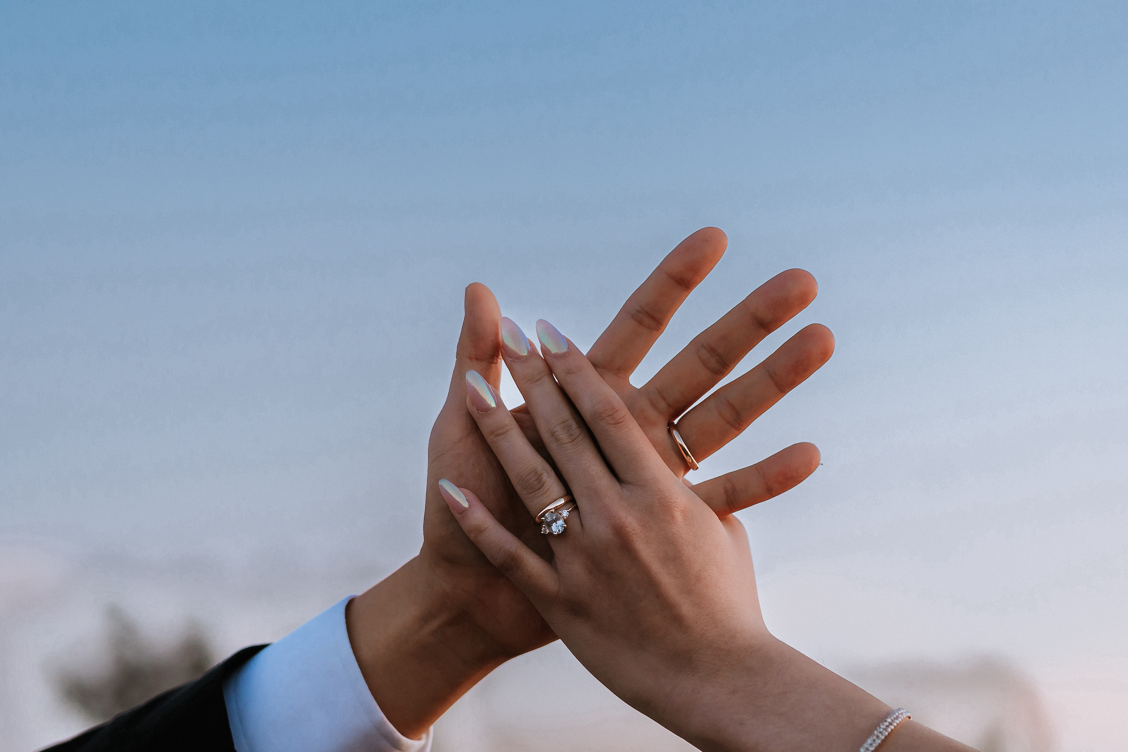 Close-up of bride and grooms hands showing their wedding rings with the blue sky in the background.