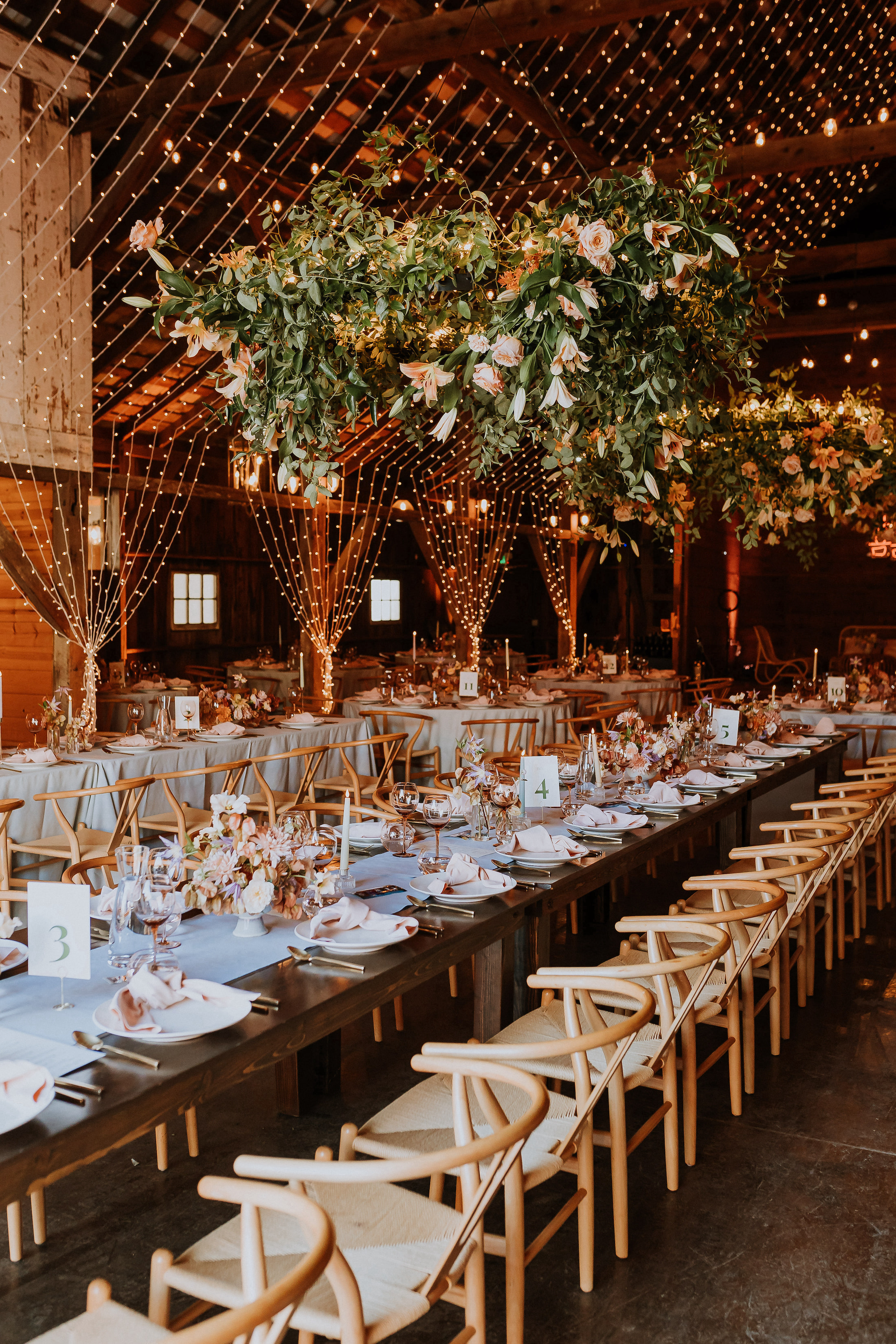 Barn wedding reception adorned with hanging lights and floral installations. 