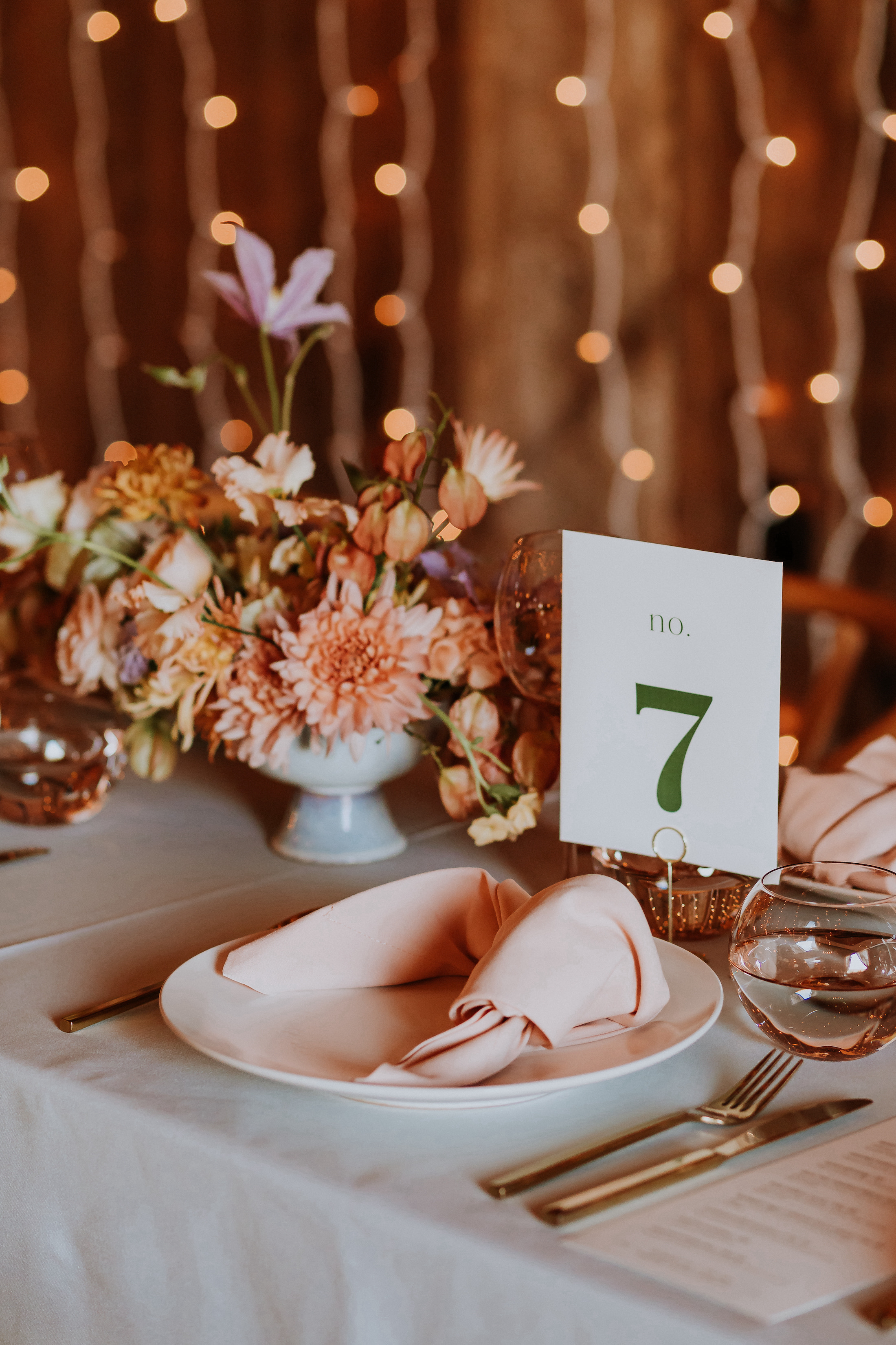 Table setting with a floral arrangement and a table number that reads "7" with twinkle lights in the background.