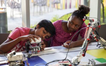 Two kids playing with robotics on a tabletop.