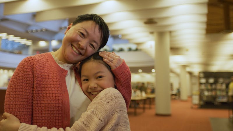 A woman and child smile and embrace in the library. 
