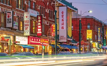 Toronto's Chinatown on Spadina Avenue, featuring storefronts and bright signage, and a timelapse image of the headlights of cars as the go down the busy street.  