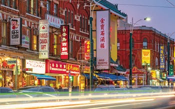 Toronto's Chinatown on Spadina Avenue, featuring storefronts and bright signage, and a timelapse image of the headlights of cars as the go down the busy street.