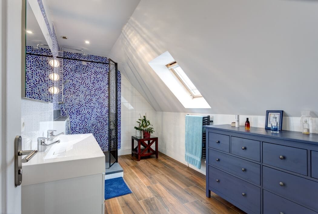 Salle de bain ambiance bord de mer avec commode bleue, parquet pont de bateau, et douche à l'italienne