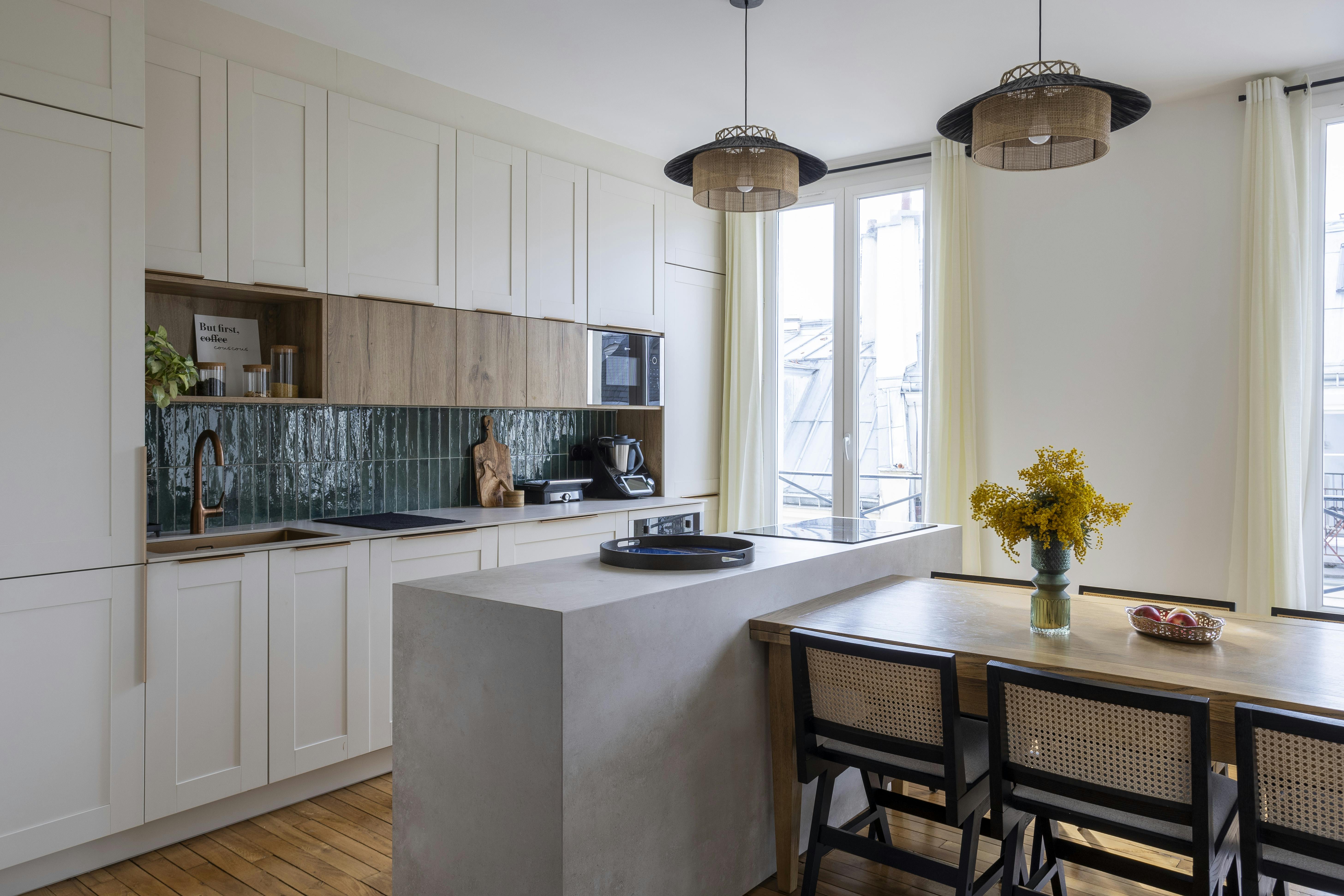 Une cuisine lumineuse et naturelle avec ilot en béton, façades crème et crédence vert profond.
