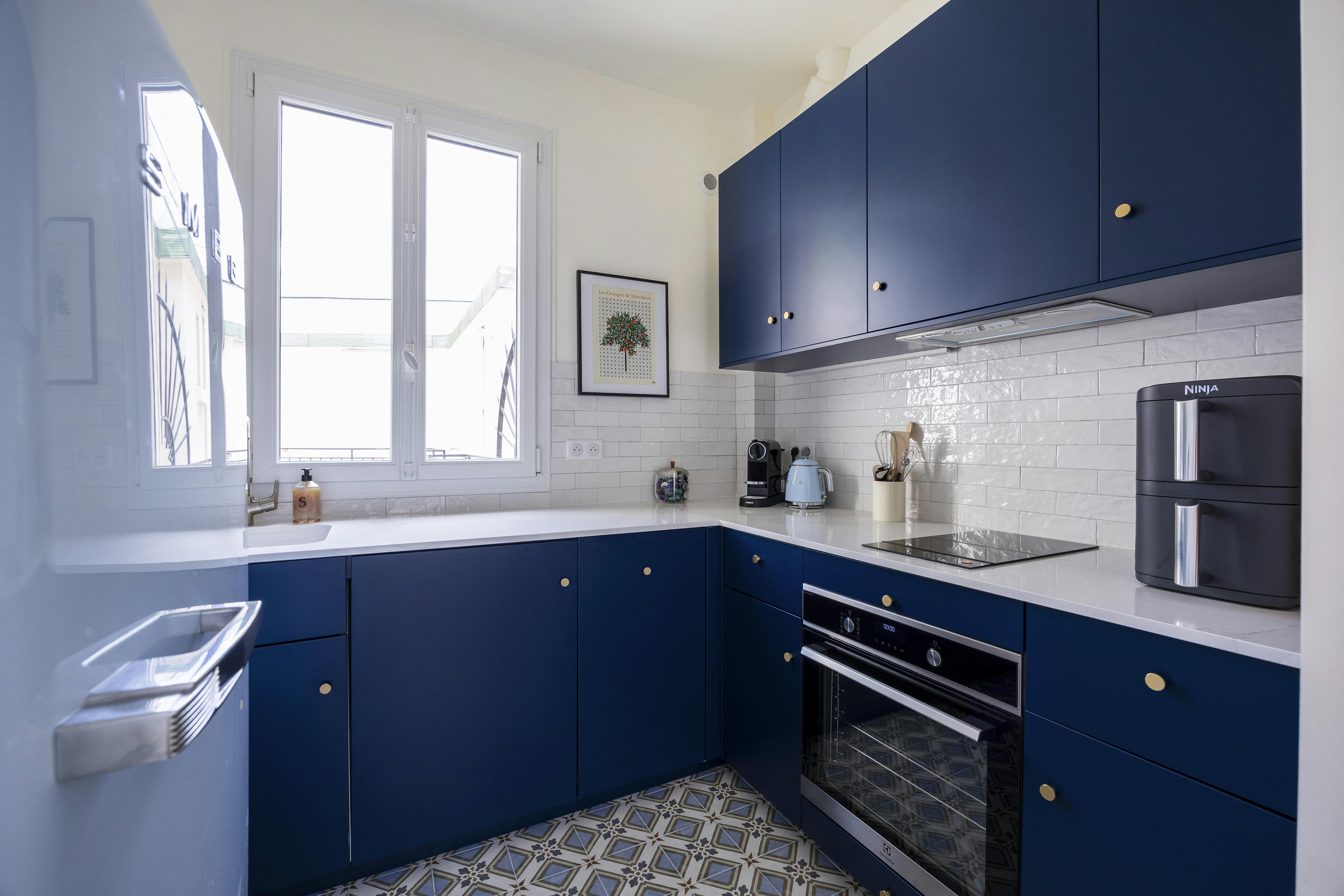 Une cuisine bleu profond au design épuré, baignée de lumière naturelle.