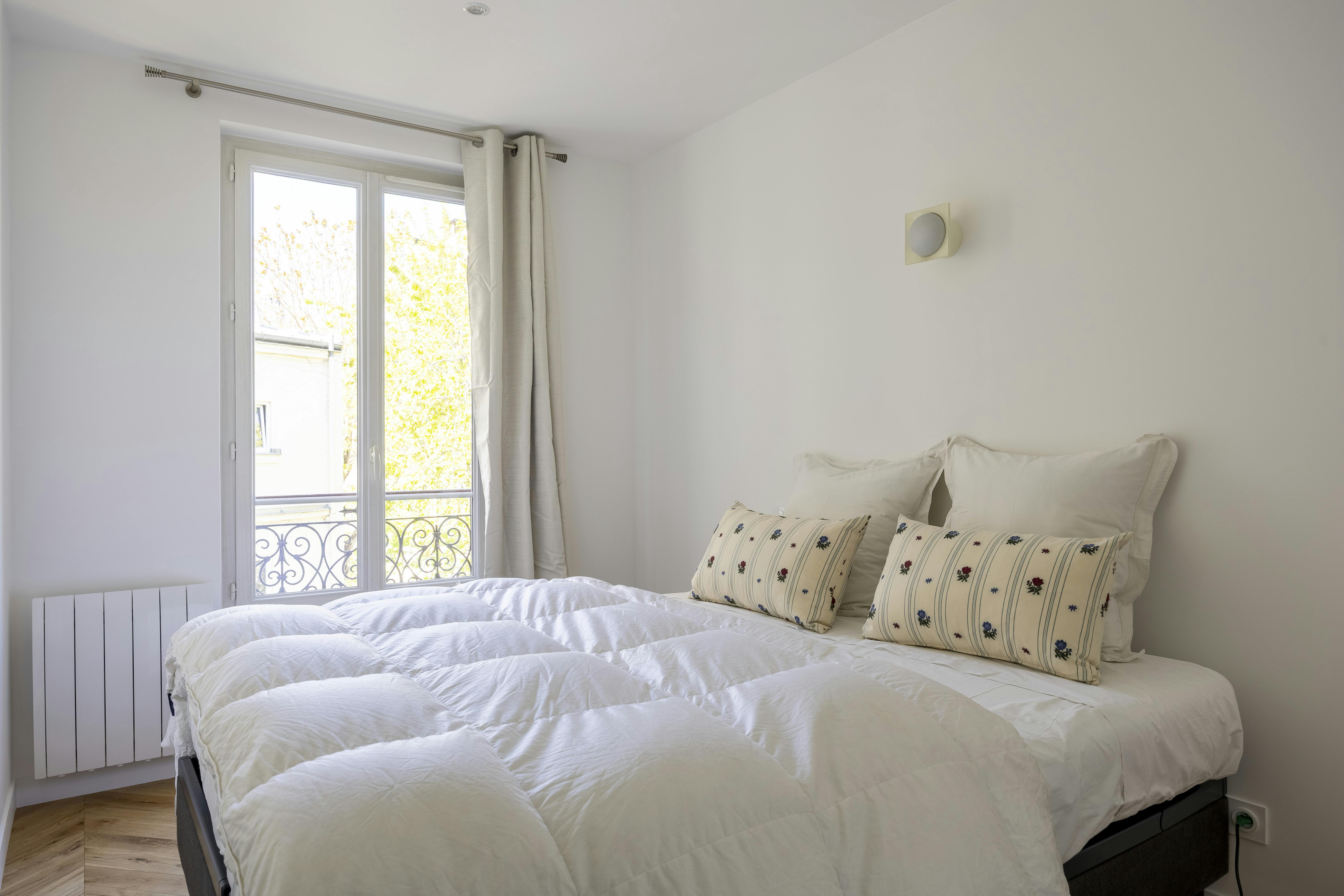 Chambre lumineuse et épurée avec literie blanche et coussins décoratifs.