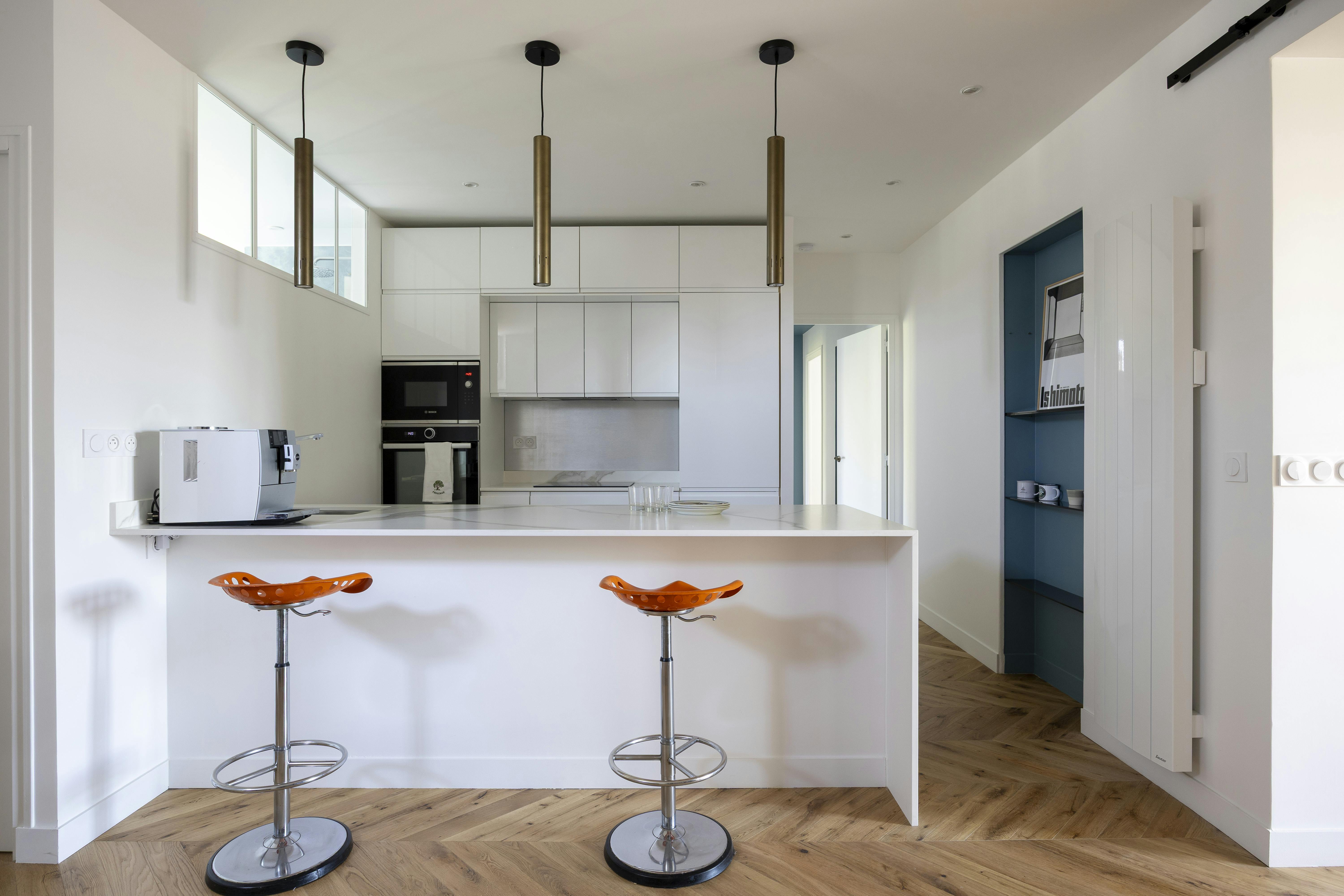 Cuisine moderne avec îlot blanc et tabourets orange.