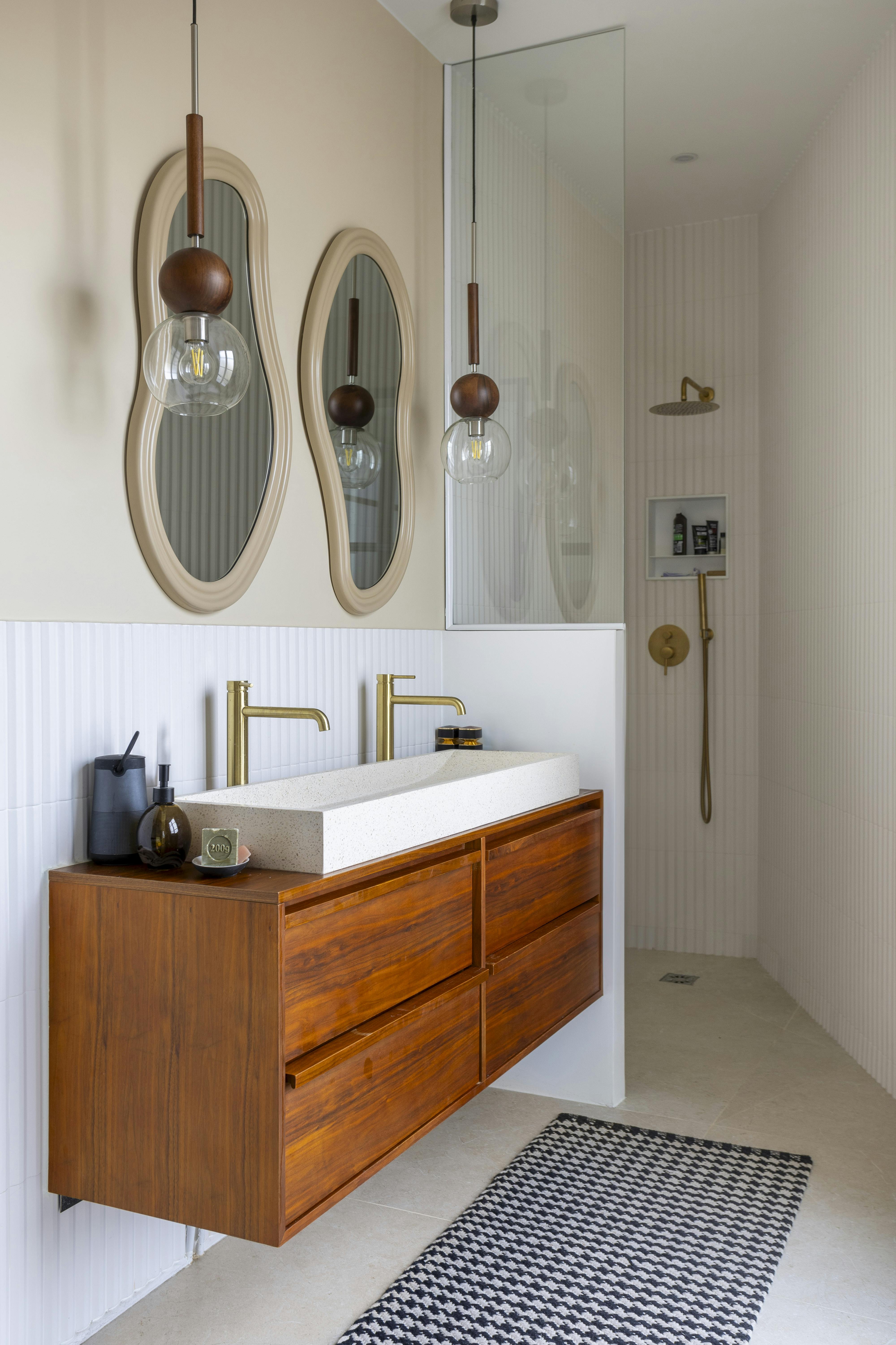 Salle de bain élégante avec meuble vasque en bois, miroirs organiques et robinetterie dorée.