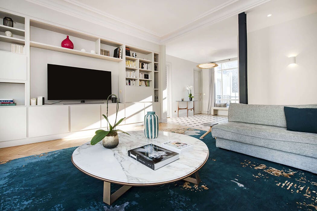 rénovation salon haut de gamme avec tapis bleu vert, canapé gris clair, bibliothèque sur-mesure