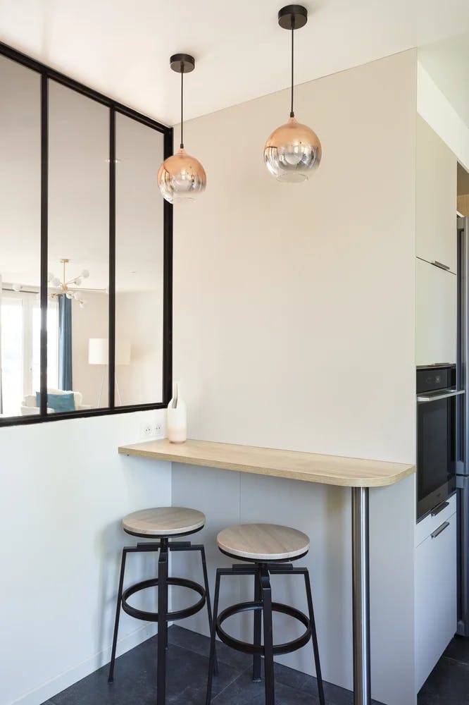 Petite table comptoir avec 2 tabourets à côté d'une verrière et lampes suspendues