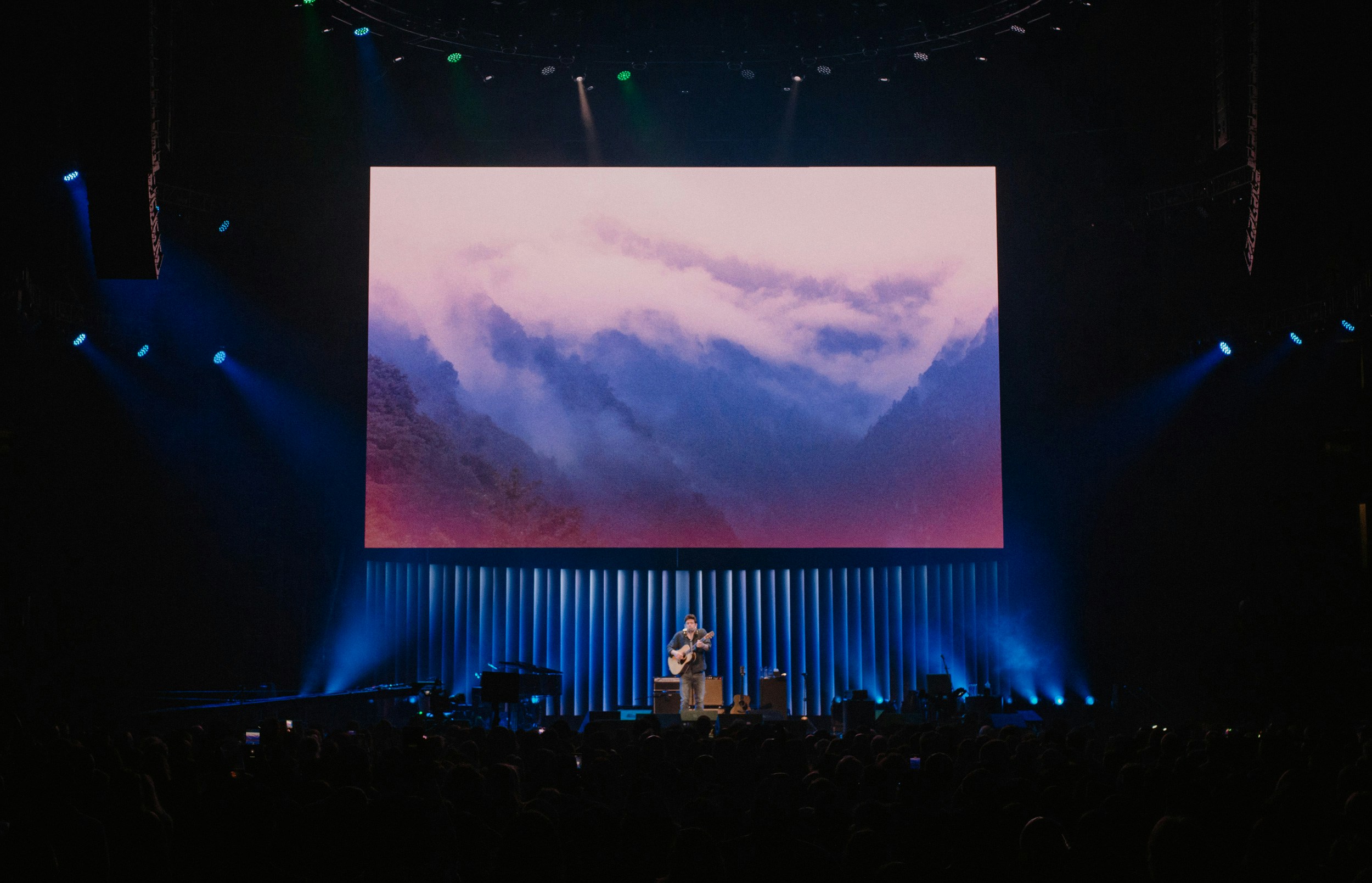 John Mayer stands on a stage holding a guitar