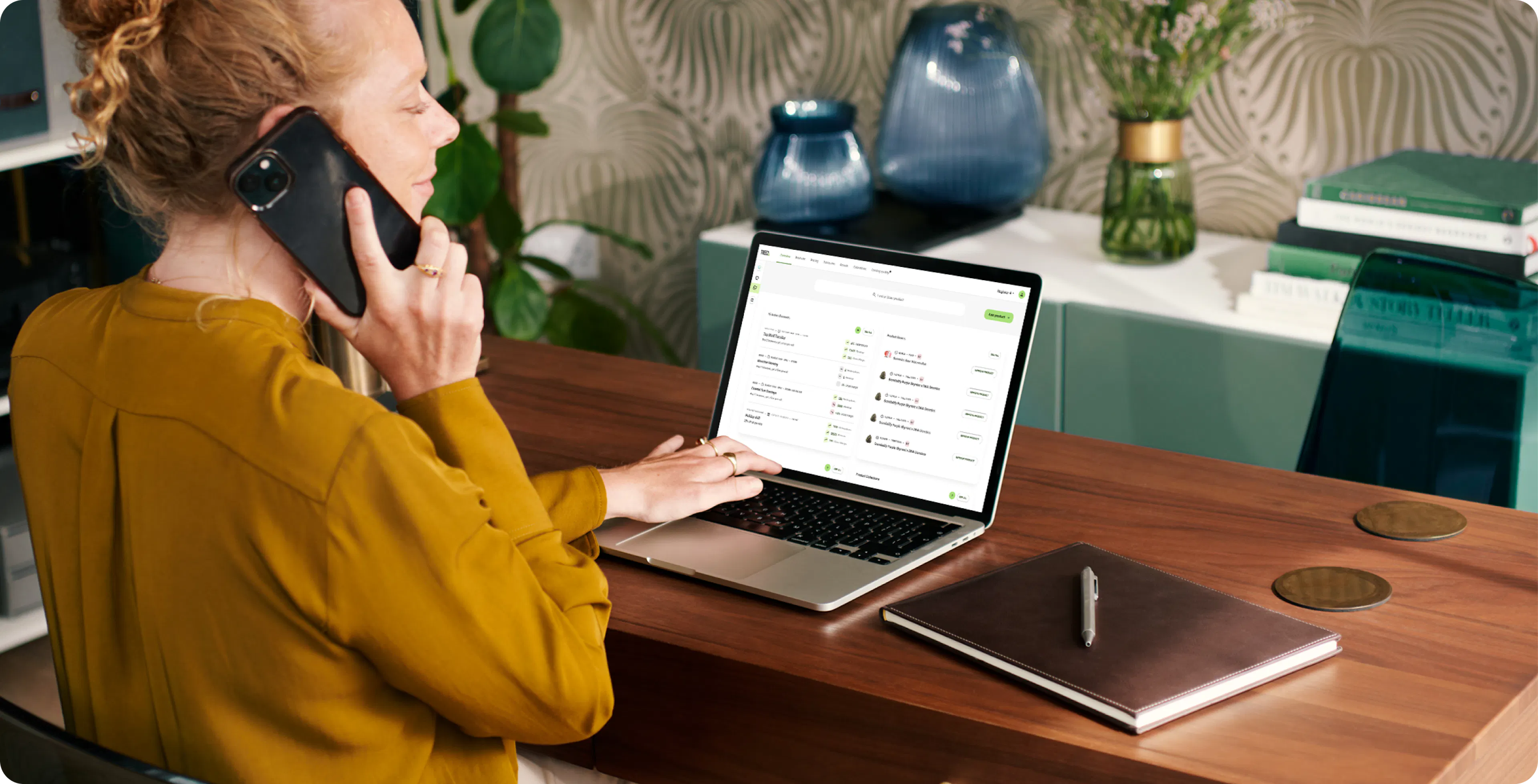 A person looks proud and confident as they hold a phone up to their ear and navigate on their computer reordering cannabis products for their dispensary