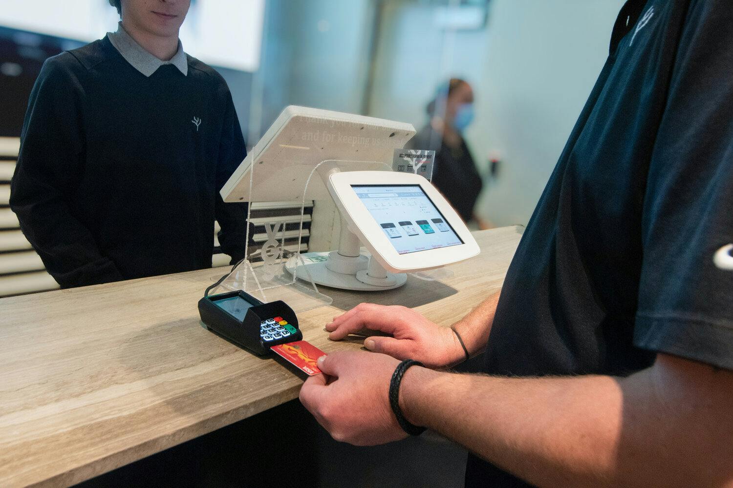 A person passes their debit card to a dispensary employee. A computer displays a POS system with analytics, roles, stores and users.