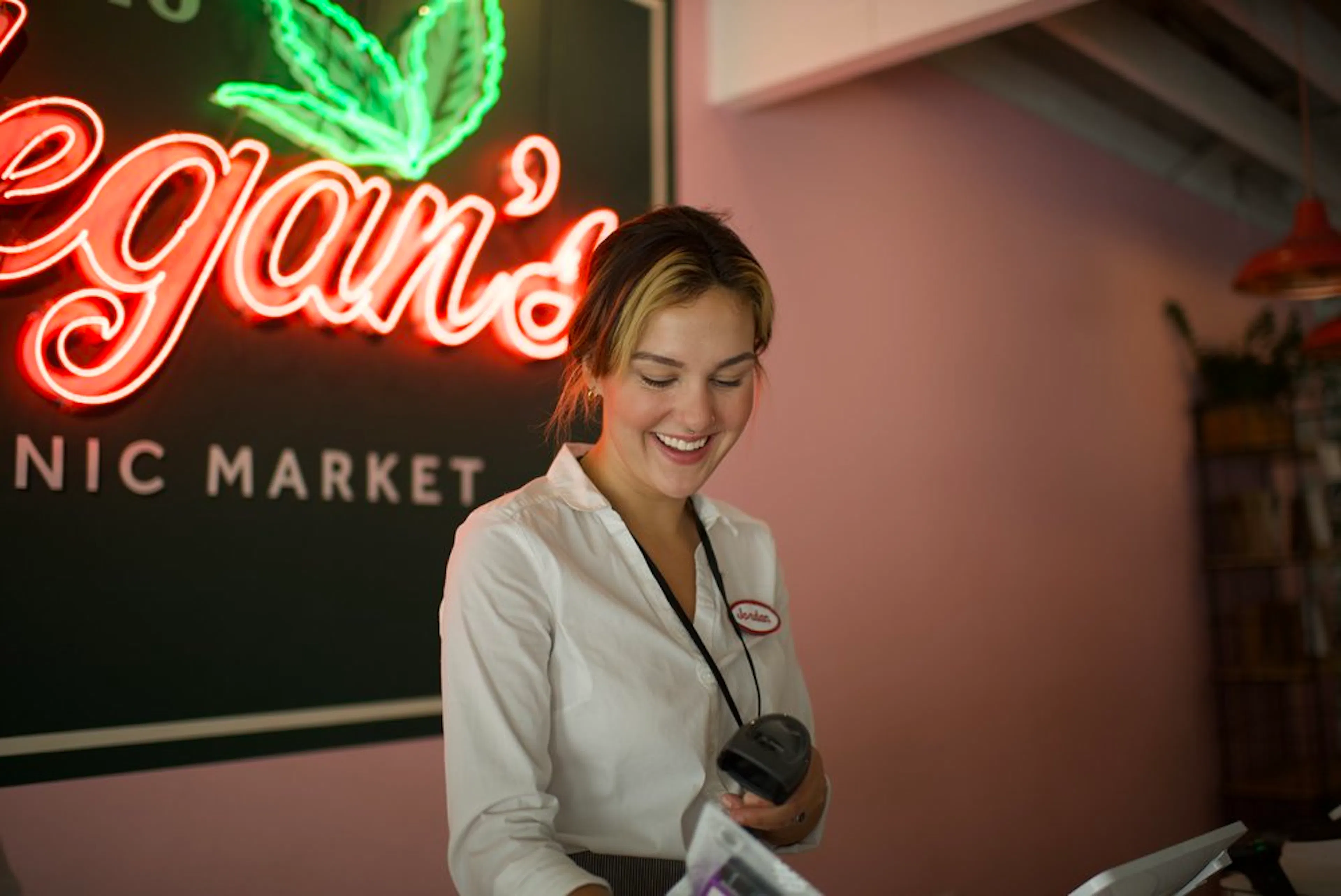 A smiling budtender scans product in front of a neon sign that says Megan's Organic Market