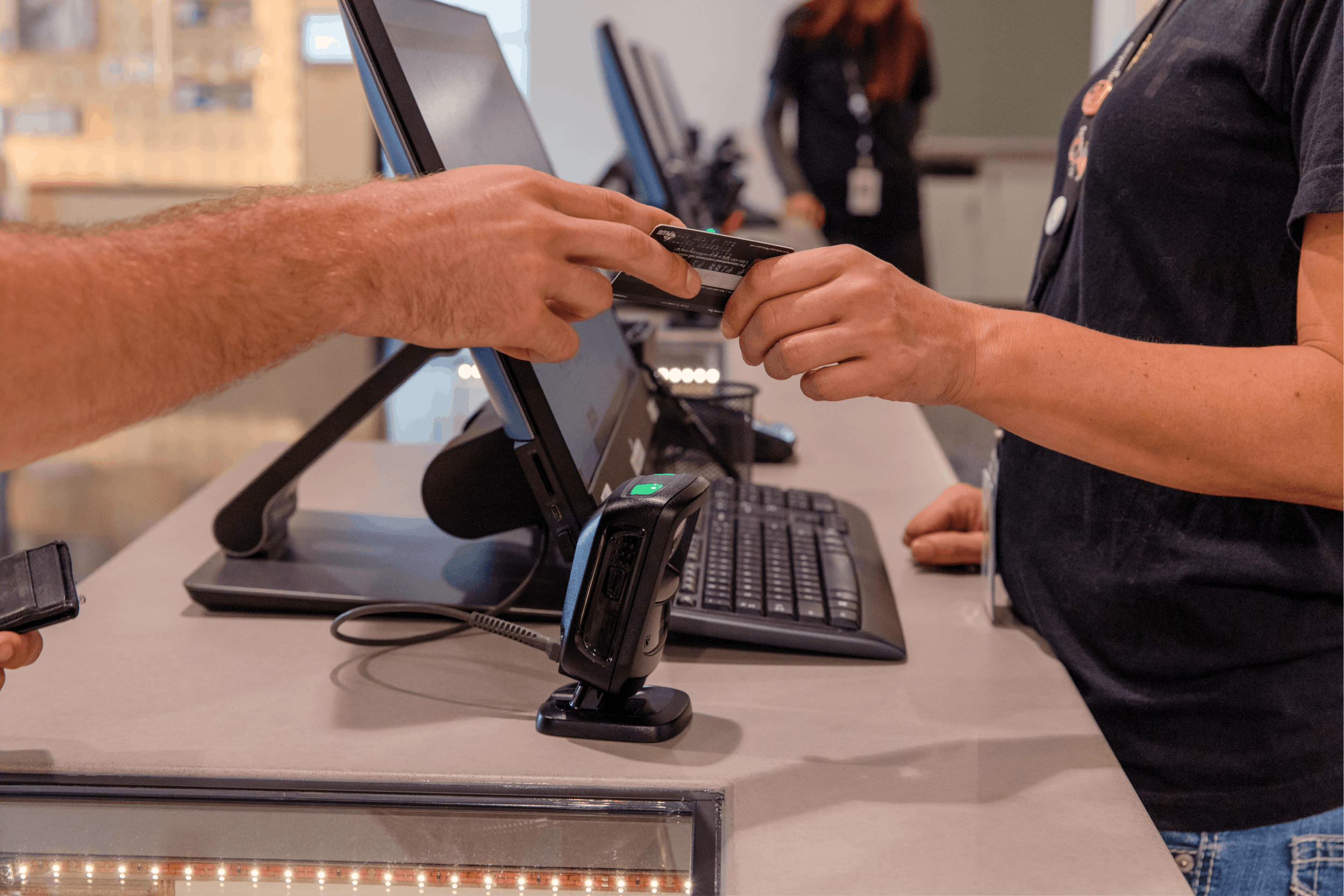 Two hands are shown surrounding a cannabis POS. One hand passes a debit or credit card to the sales associate budtender, to purchase cannabis products in a dispensary without using cash
