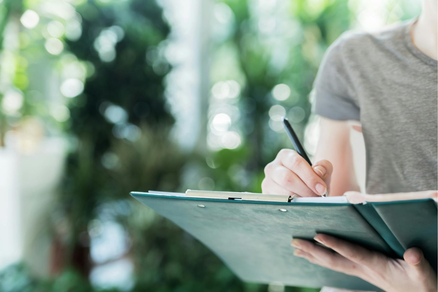 A person holds a binder with a checklist on it, and checks off opening and closing duties for their cannabis business