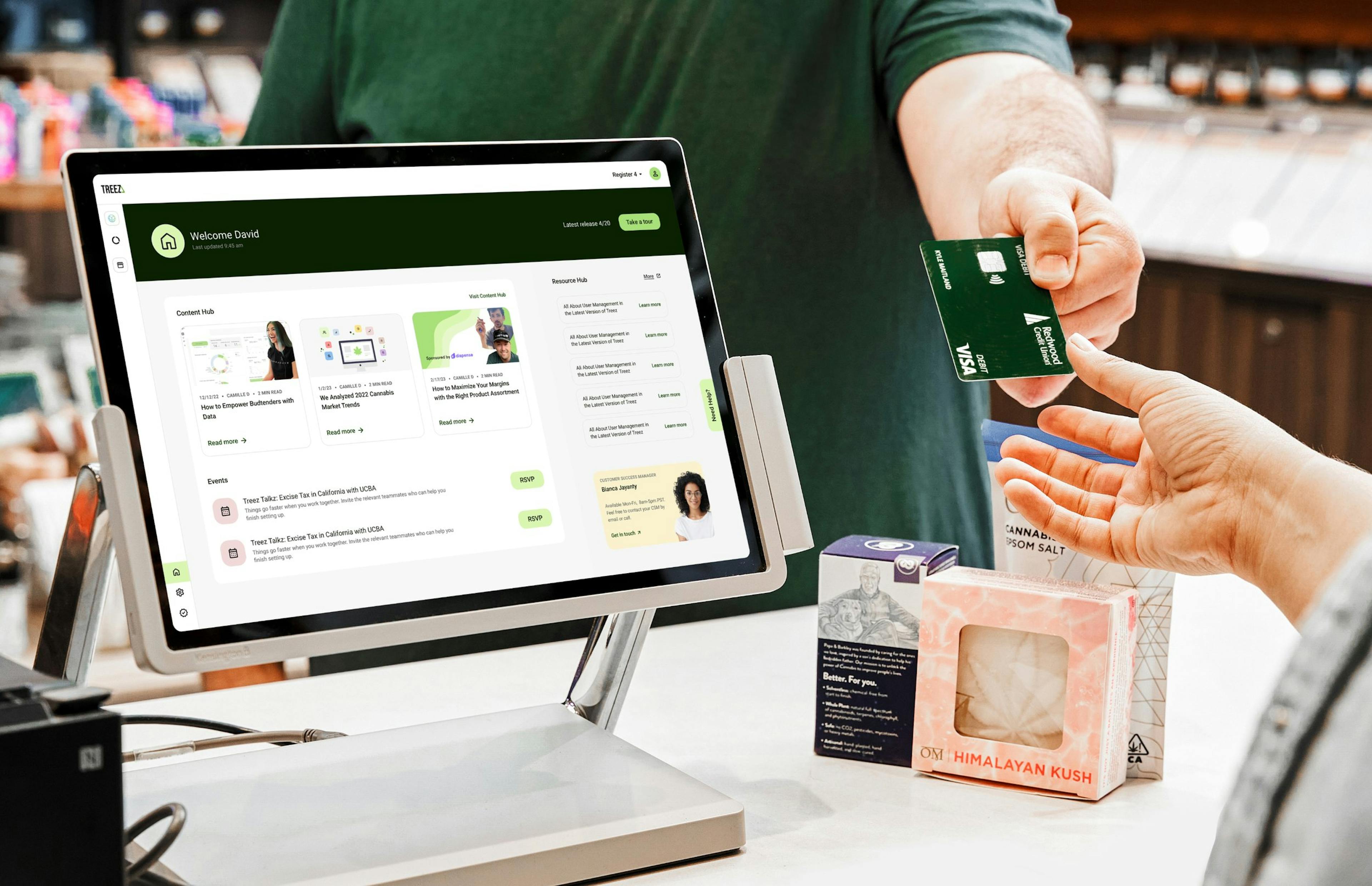 Two hands and a point of sale system are shown as a customer purchases some cannabis products at a dispensary