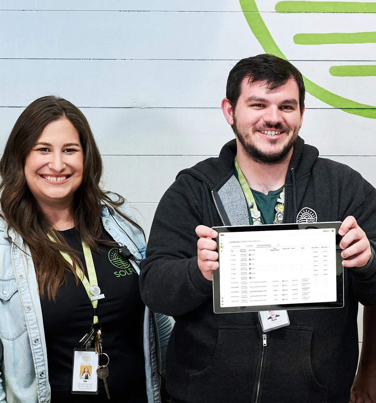 Two smiling budtenders hold up a iPad with Treez point of sale software up on the screen