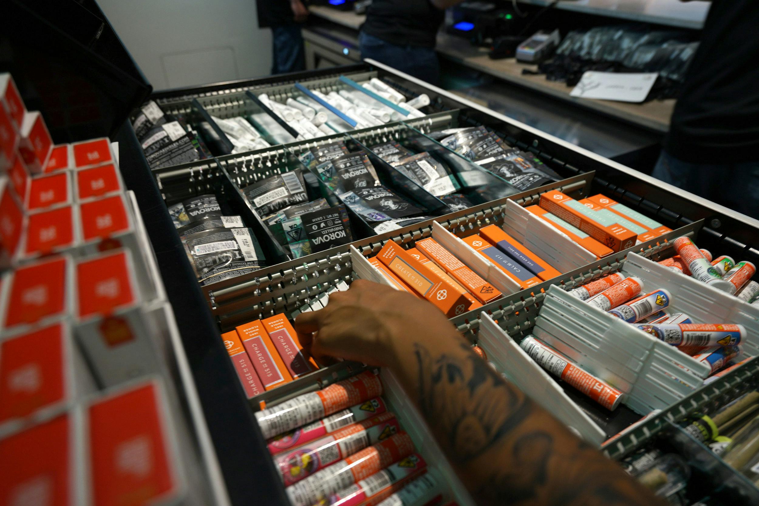 A hand reaches over a drawer full of cannabis products, all organized with separators and by category in order to maximize Metrc compliance