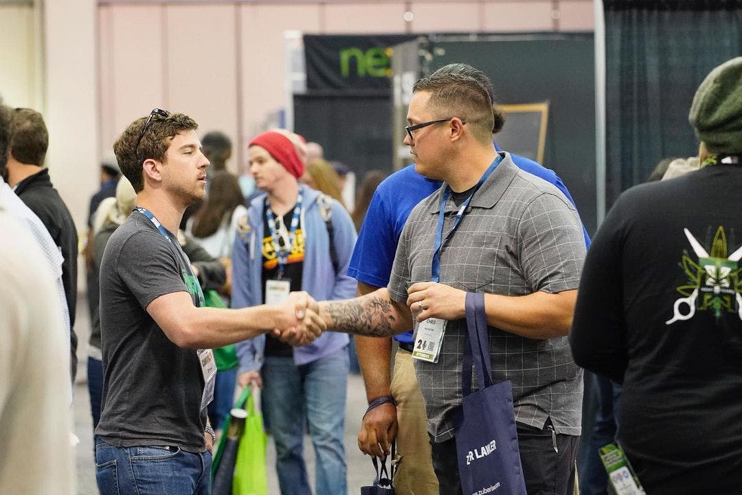 Two people in casual attire shake hands on the floor of CannaCon, a cannabis conference in Long Beach California