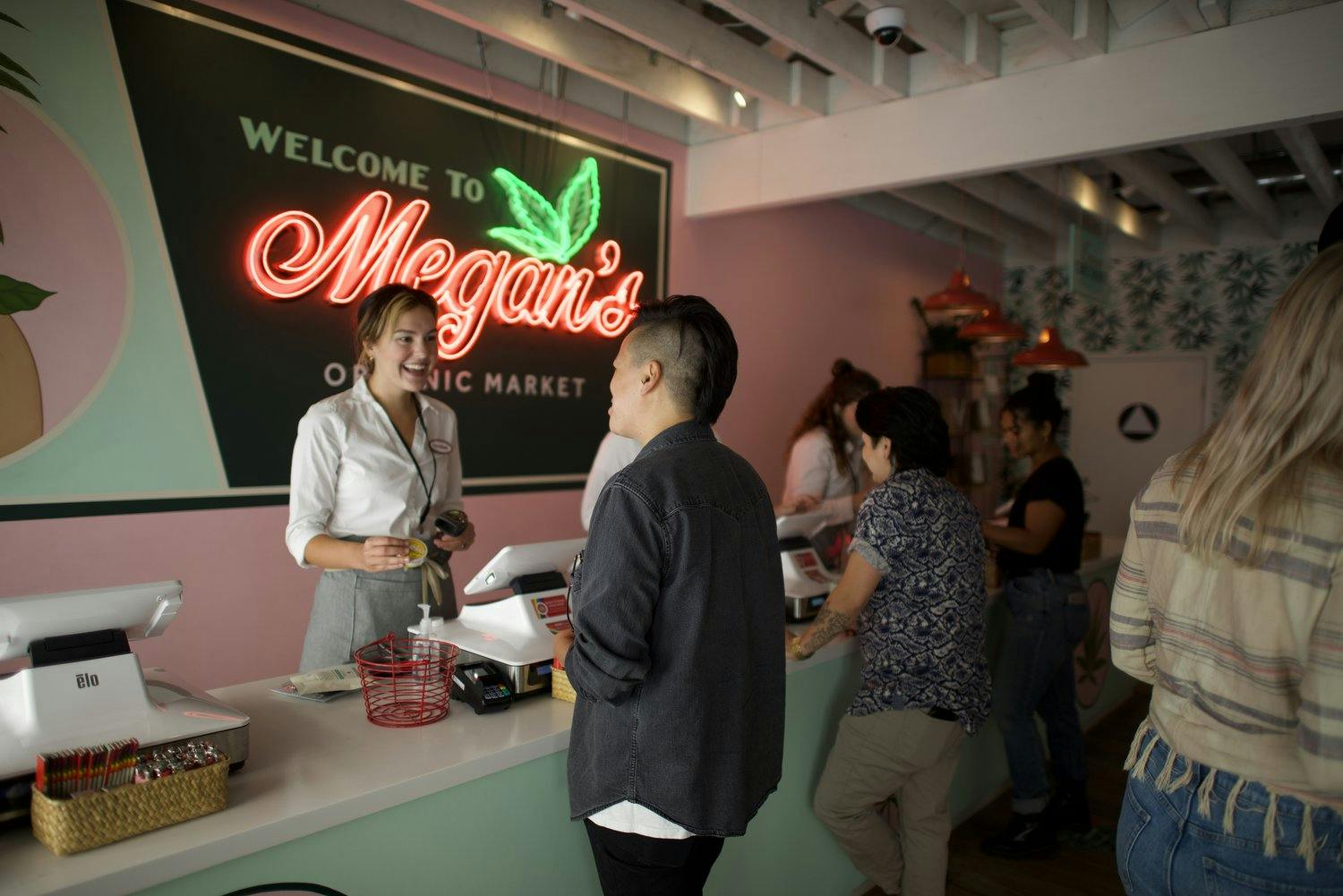 A smiling budtender completes a purchase that a customer has brought to the counter at Megan's Organic Market dispensary