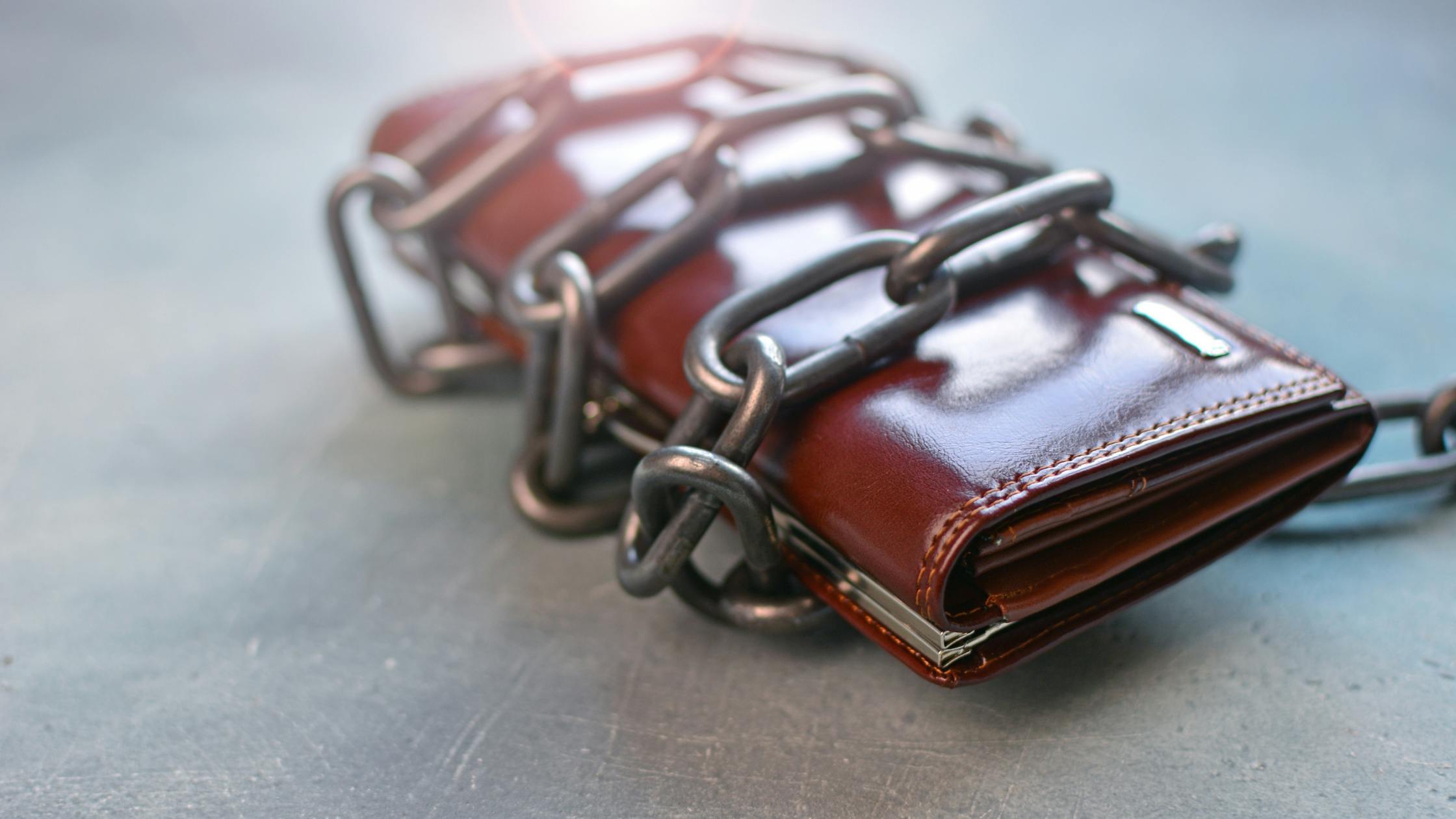 A leather wallet sits on a counter, with chain wrapped around it, preventing anyone from opening the wallet