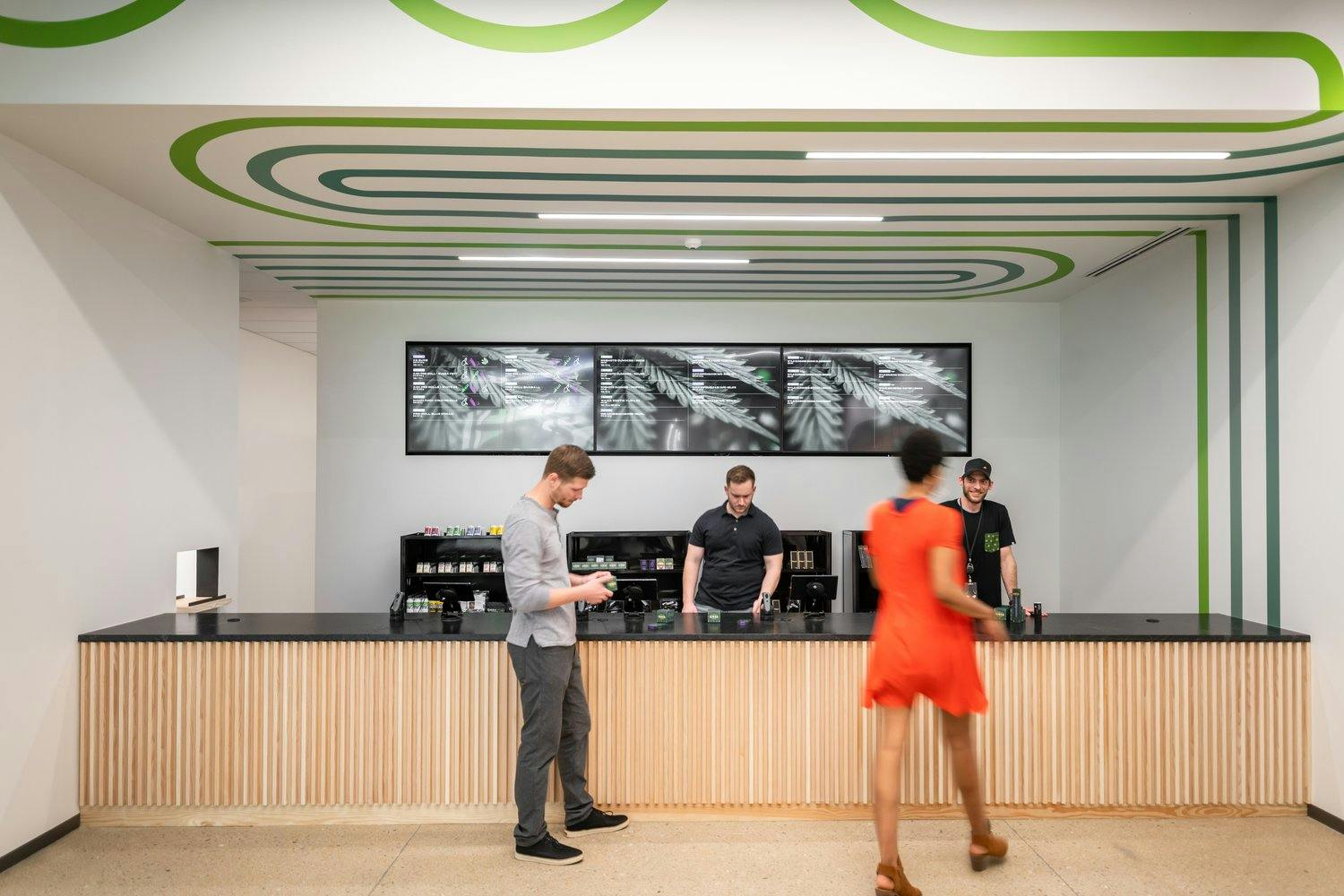The interior of a vibrant and fun dispensary - the menus are digital signage and the ceiling is painted with energizing swirls. Budtenders stand behind the counter waiting to help the shopping patrons